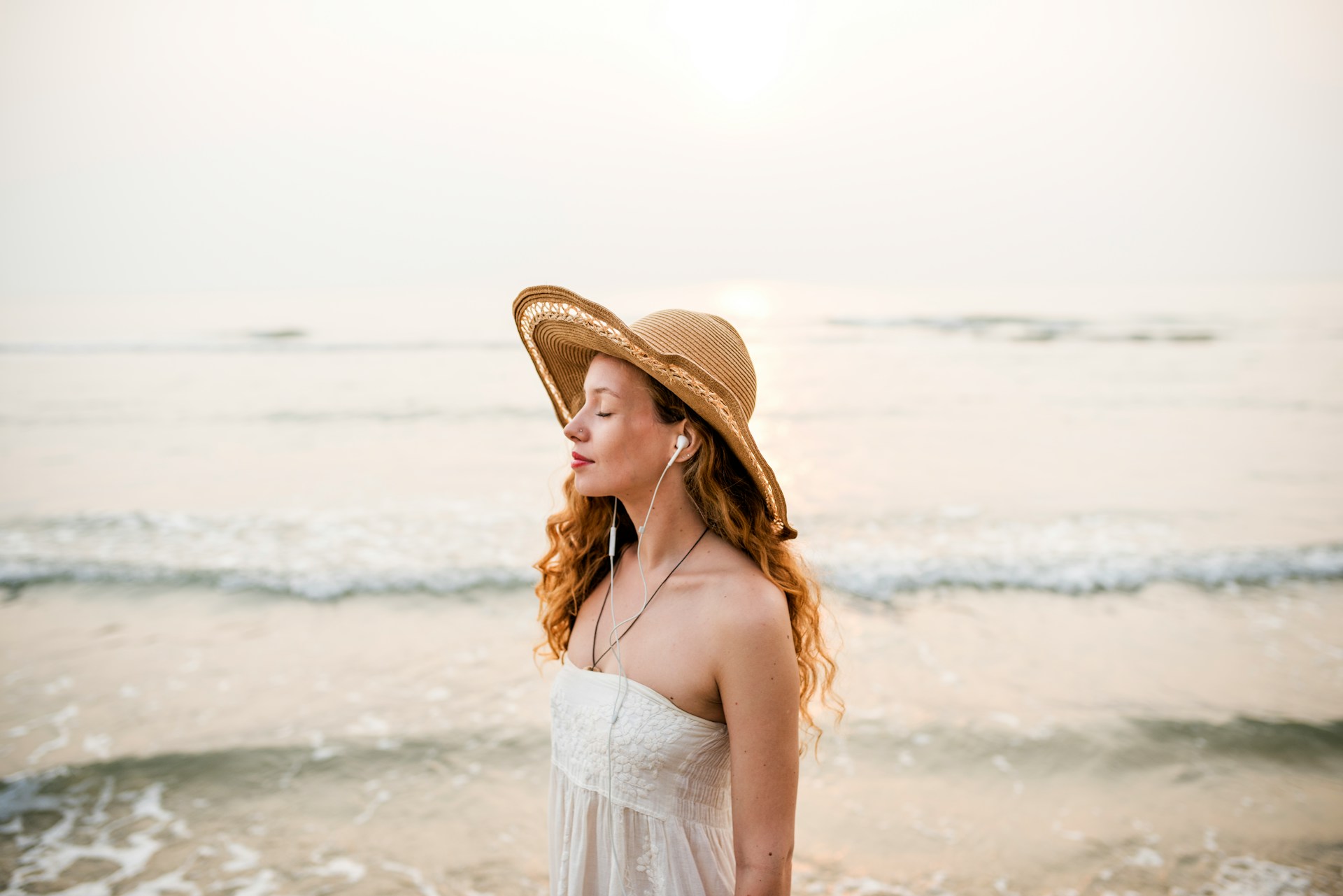 A woman listening to music peacefully at the beach, eyes closed, finding calm and emotional stillness