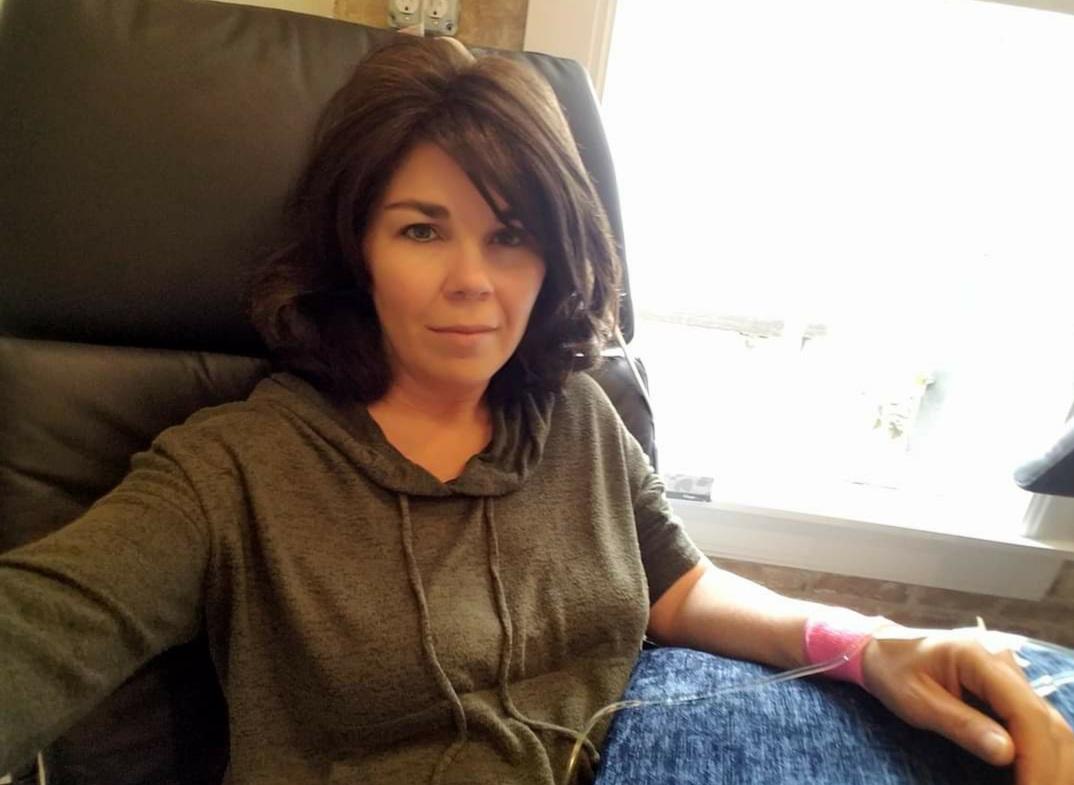 Woman receiving treatment for chronic illness in a medical setting, wearing a gray hoodie, with an IV line visible on her arm, emphasizing the journey of health recovery.