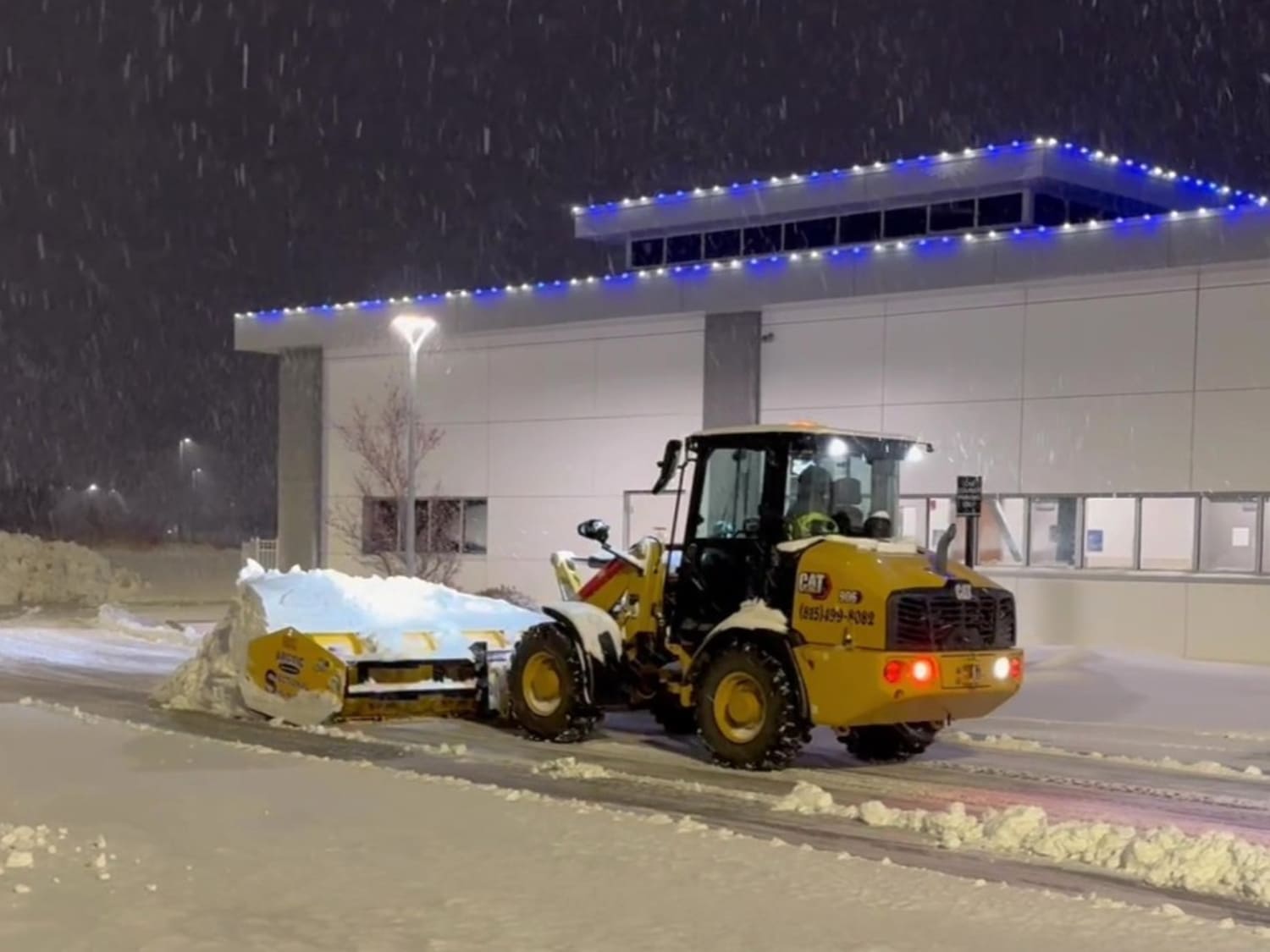 CAT loader clearing snow from a commercial parking lot at night during a snowstorm