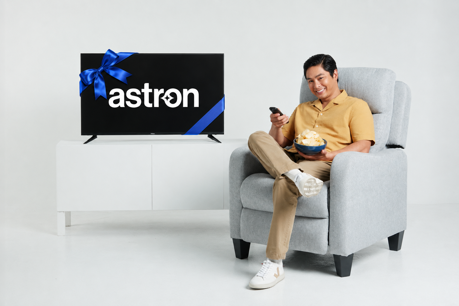 Coco Martin relaxing in armchair with Astron TV gift wrapped with blue ribbon, holding remote and chips