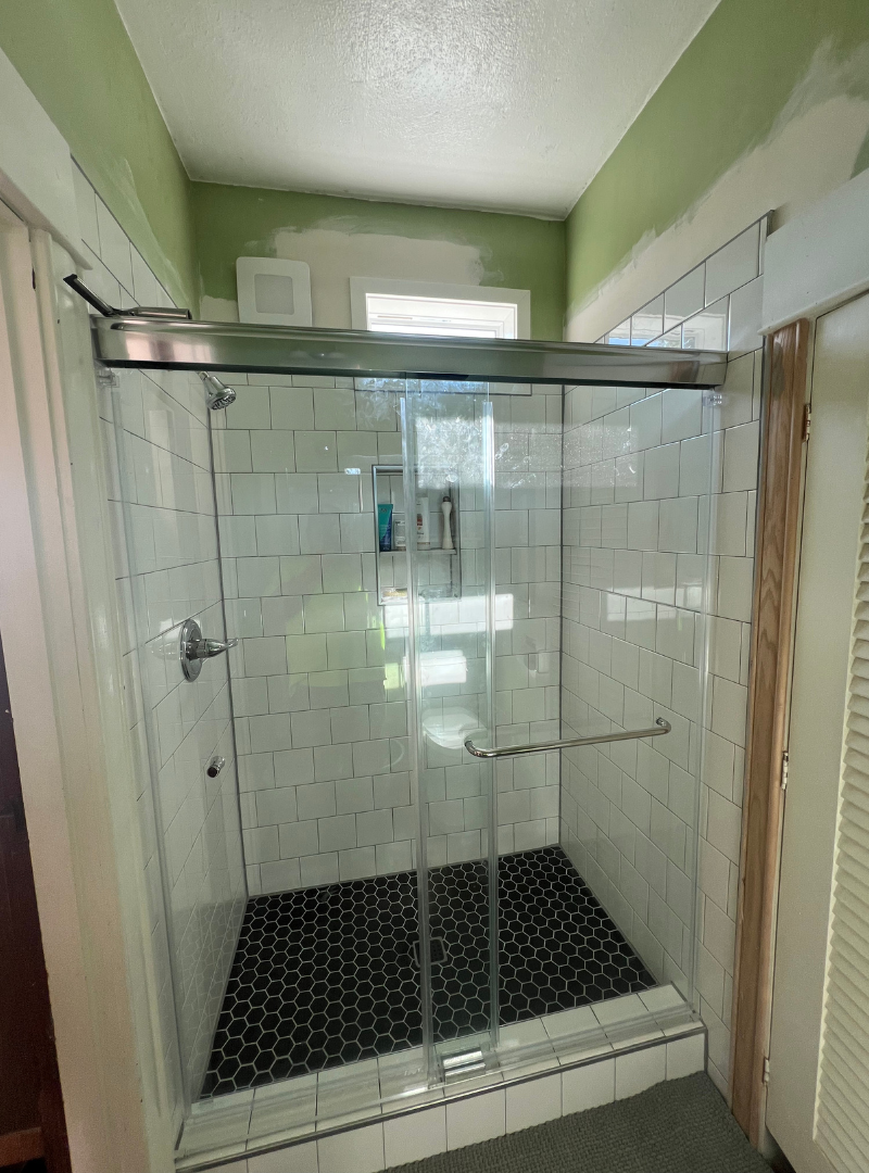 Completed bathroom remodel with white subway tile shower, glass enclosure, and hexagon floor tile