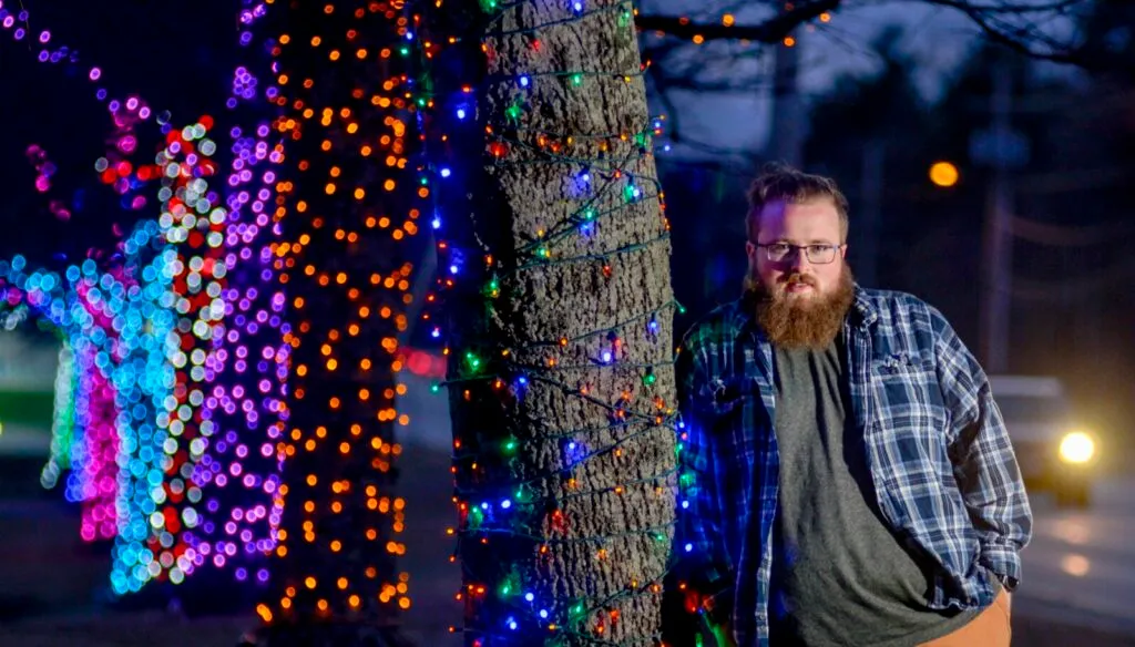 Kaleb, Owner of SkyBox Holiday & Event Lighting, beside illuminated trees