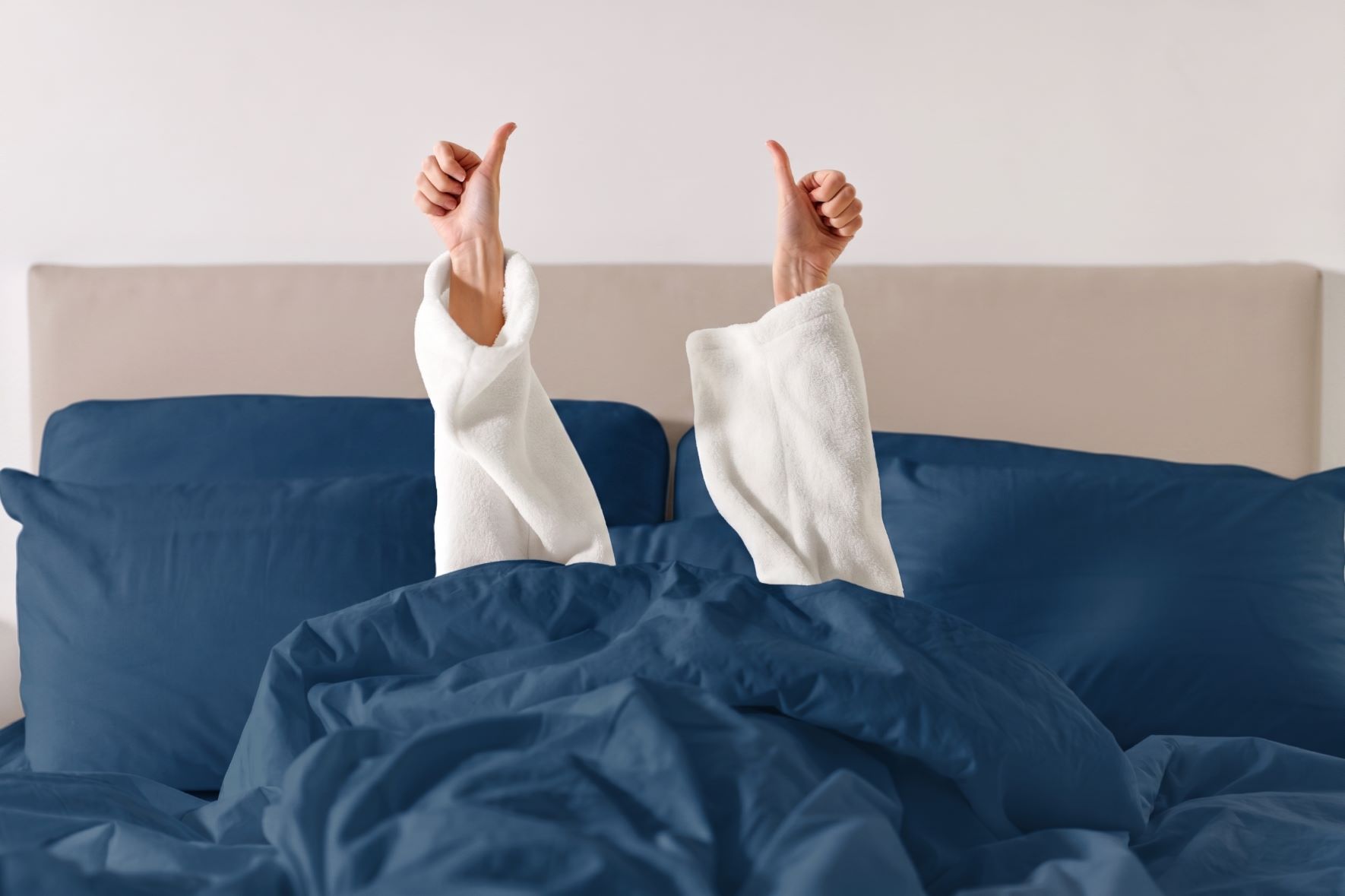 Frau reckt Daumen hoch aus dem Bett