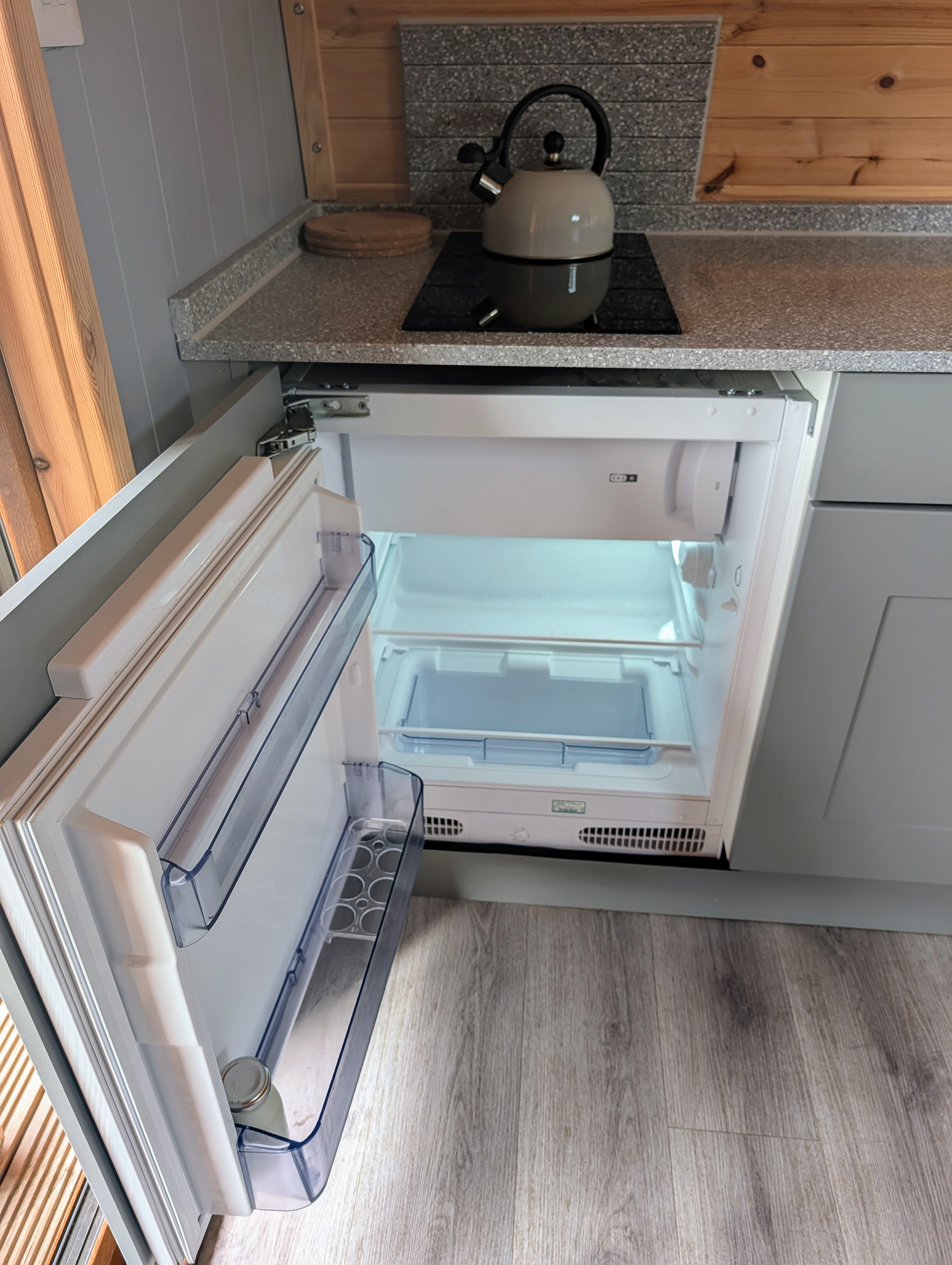 Undercounter fridge with freezer compartment open beneath the induction hob and kettle in the luxury glamping pod