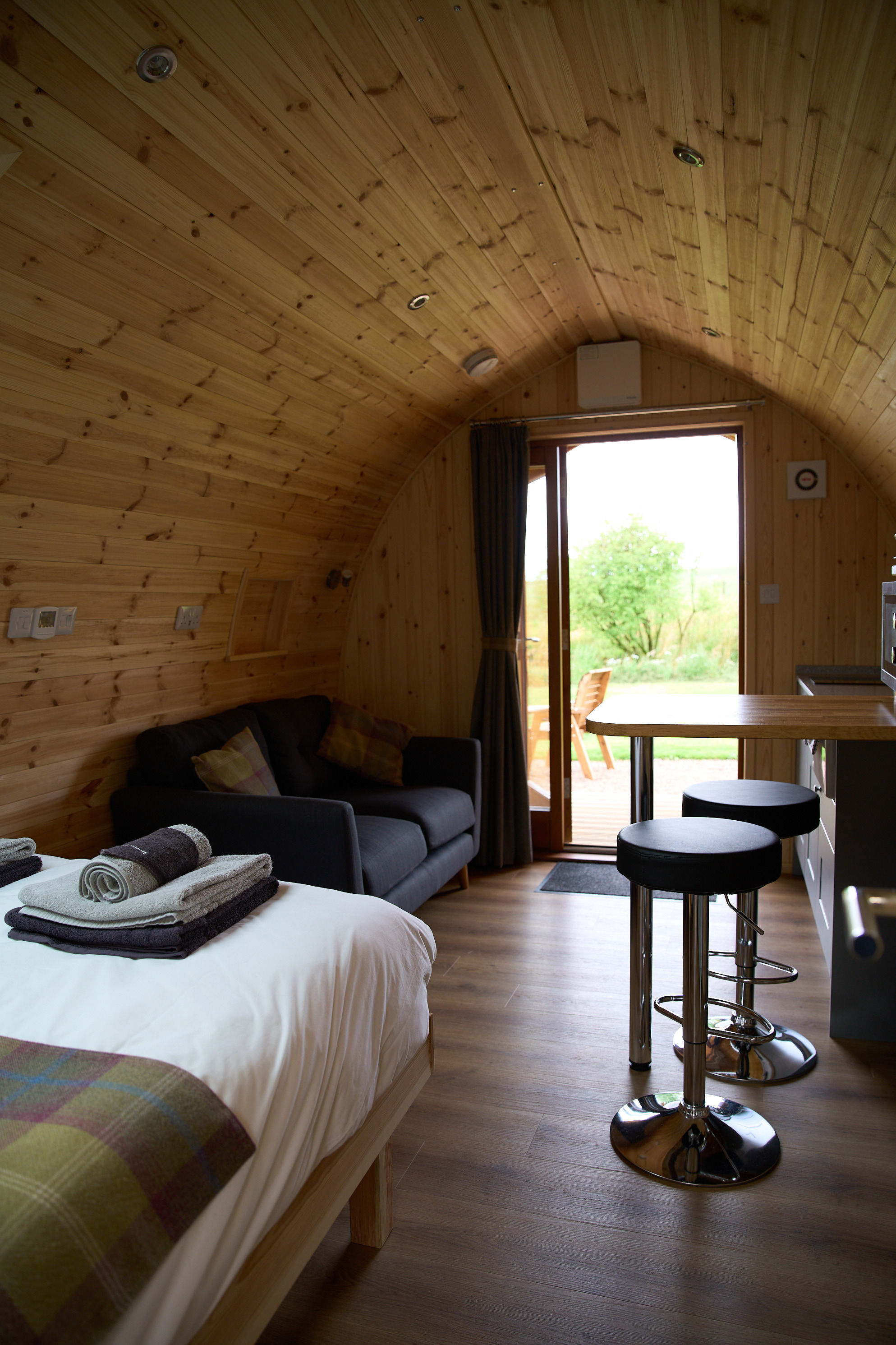 Interior view of Juniper luxury glamping pod looking towards the open door, showing comfortable seating, breakfast bar, and wooden interior at Braeview Escapes.