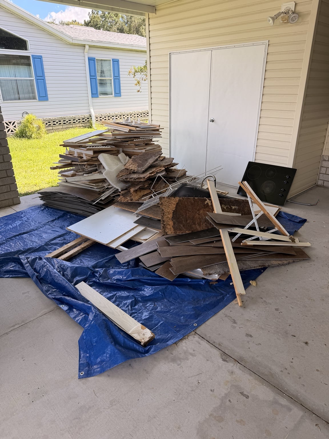 Wood, trim, and remodeling debris piled on a blue tarp beneath a covered patio.
