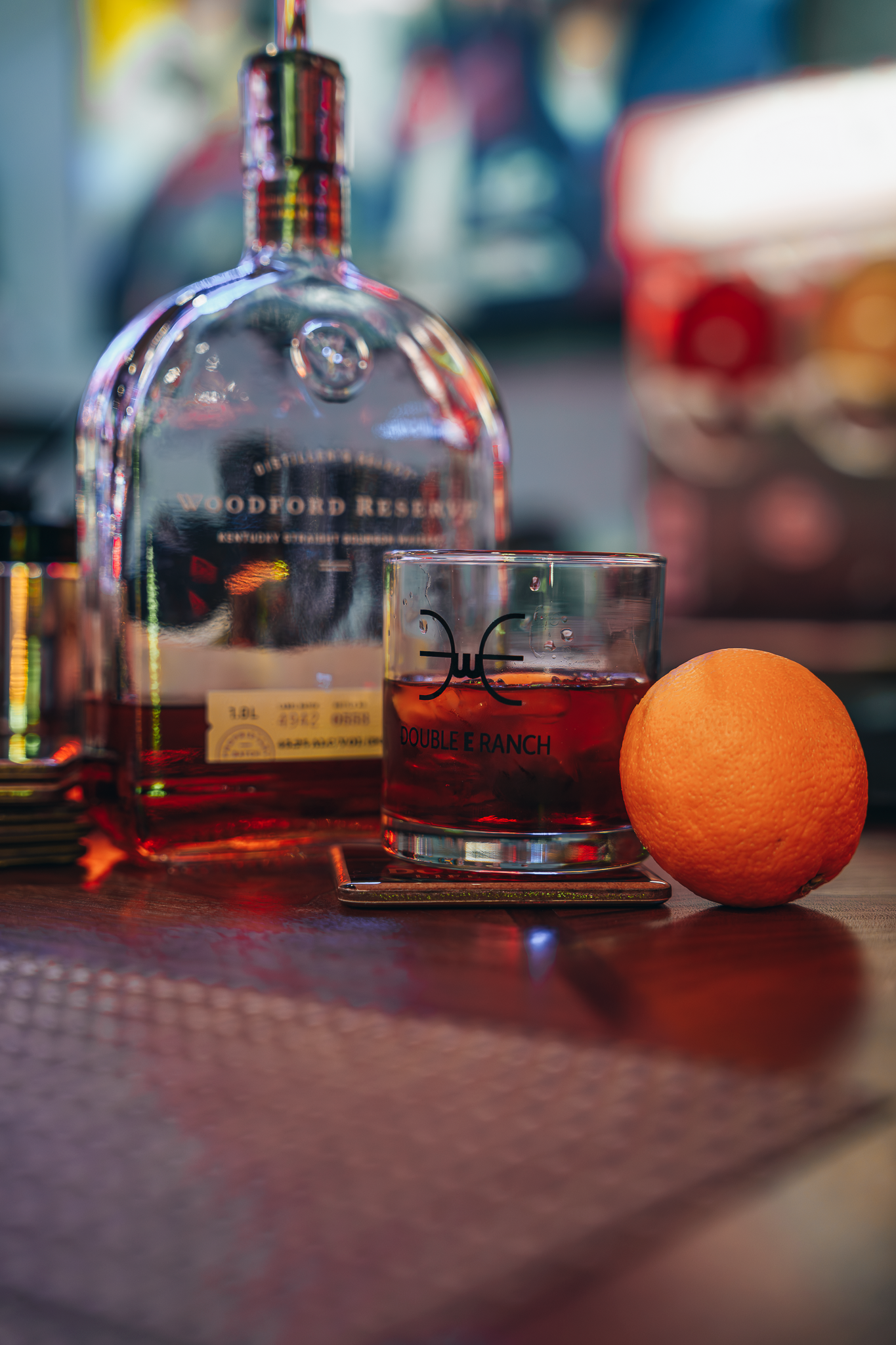 Double E Ranch branded rocks glass with orange and whiskey bottle, representing exclusive experiences and