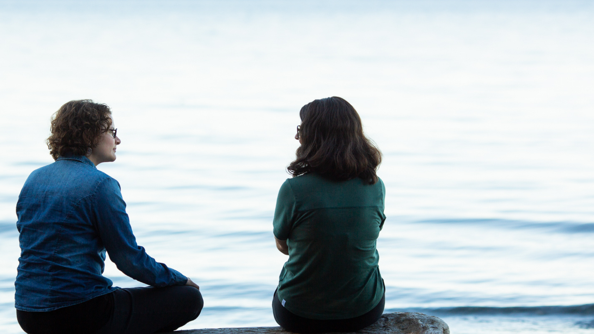 Two people sitting and talking outdoors by a lake during counselling session.