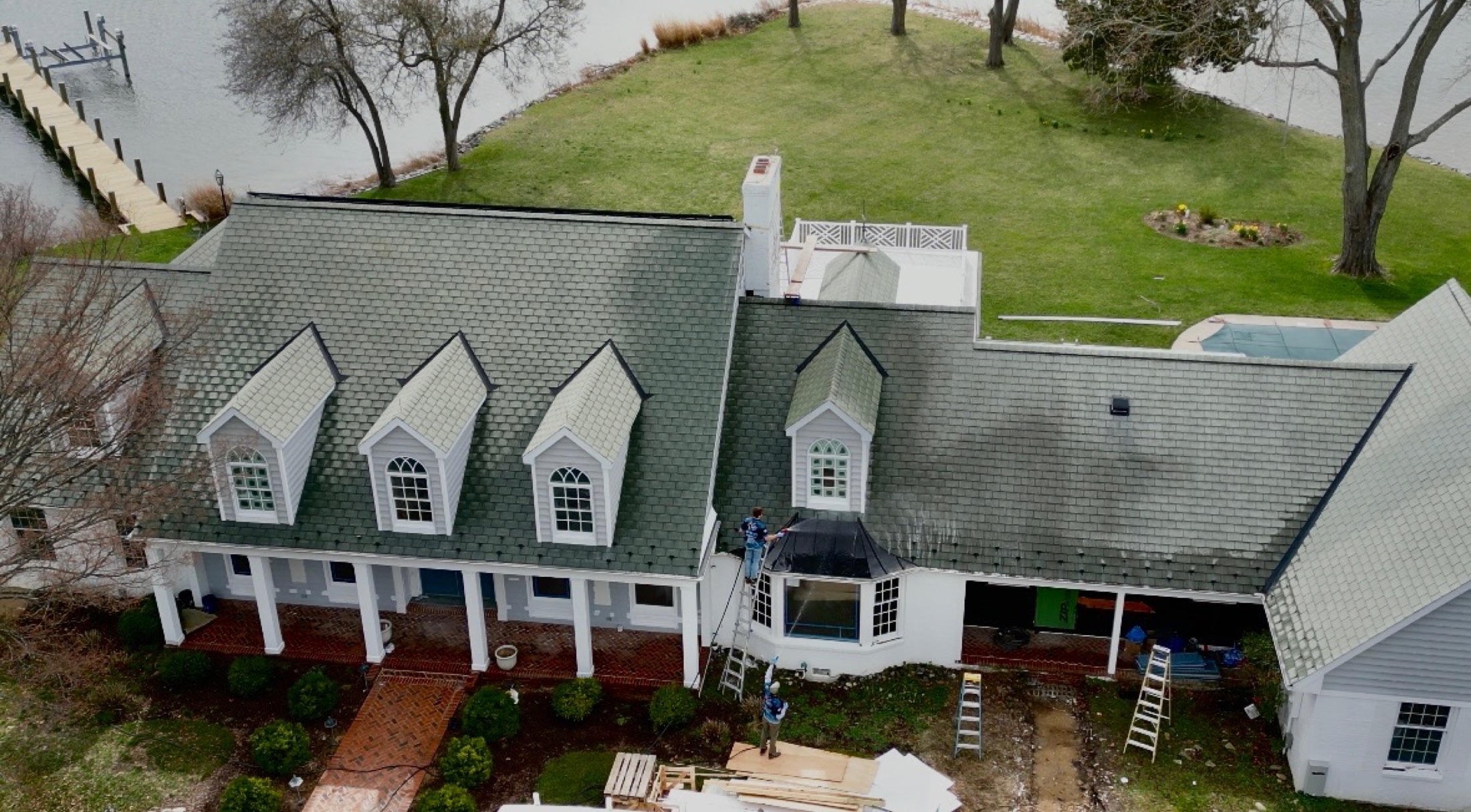 Aerial drone shot of crew soft-washing the roof of a white waterfront estate in Easton MD on Maryland's Eastern Shore by Coastal Shine
