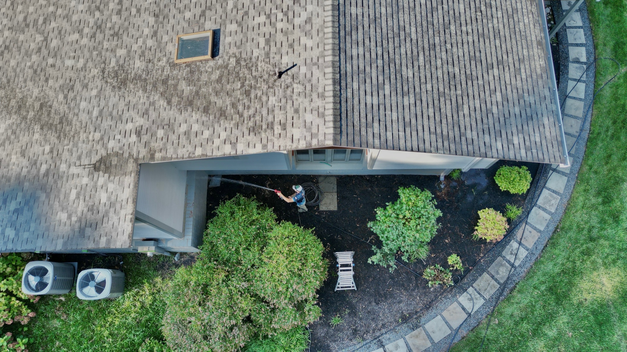 Aerial drone view of a Coastal Shine technician soft-washing a residential shingle roof and patio in Easton MD on Maryland's Eastern Shore