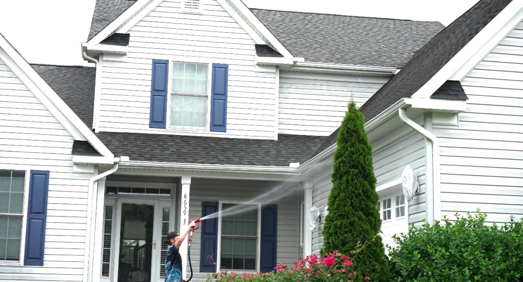 Coastal Shine technician pressure-washing white house siding with blue shutters in Easton MD on Maryland's Eastern Shore