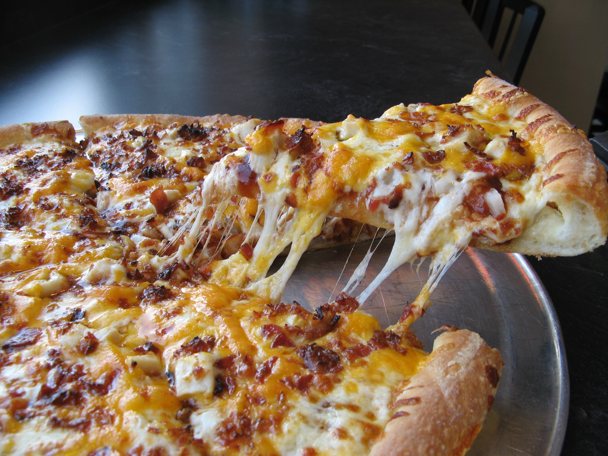 Fresh hot pizza with melted cheese being pulled from the pan
