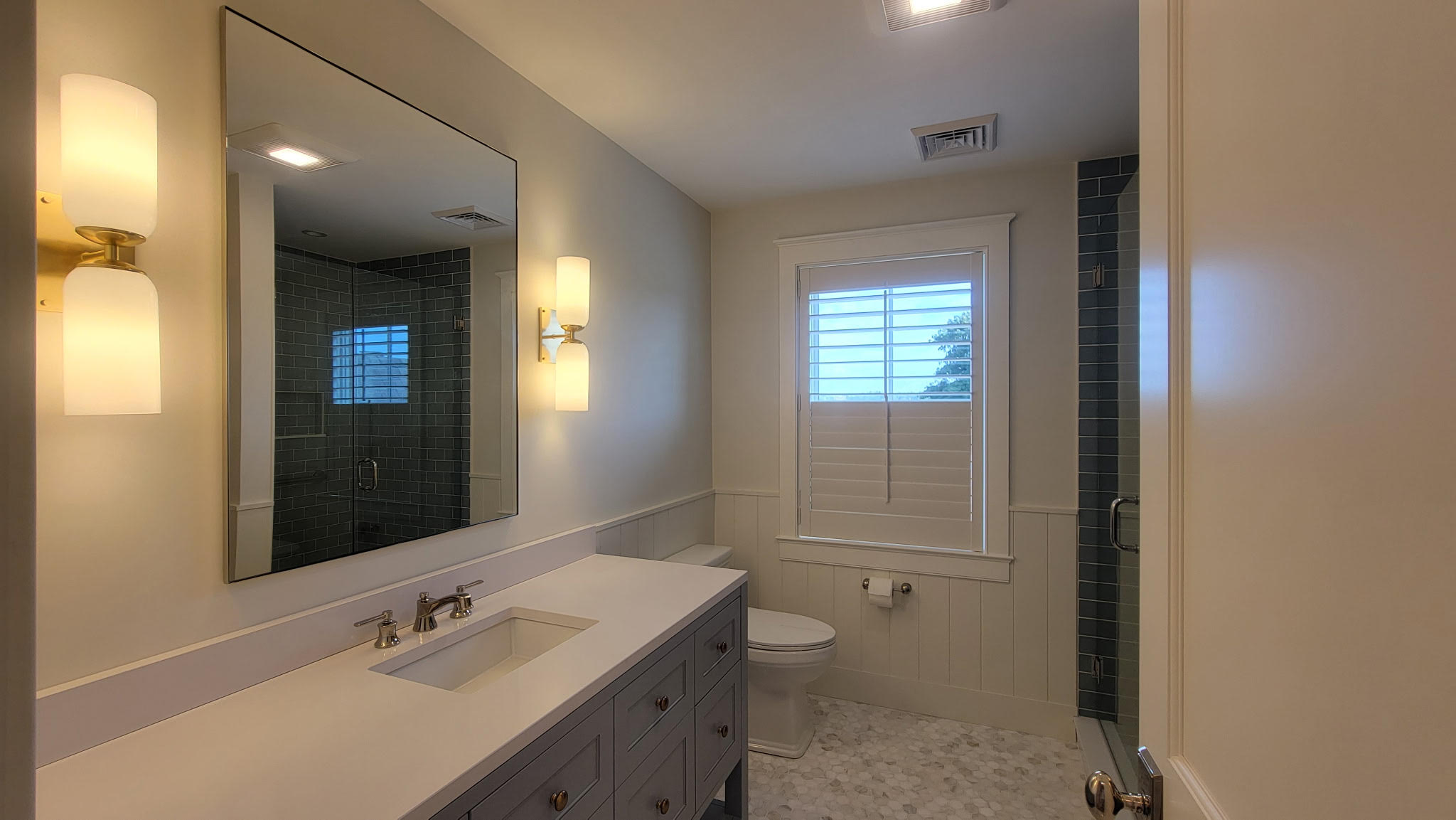 Finished residential bathroom interior featuring soft neutral painted walls, crisp white wainscoting, gray vanity, and detailed trim work by Minute Men Painters