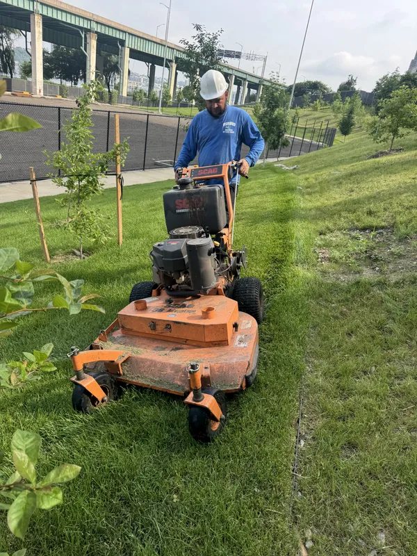 Jose Moreno crew member using a commercial stand-on mower on a sloped lawn
