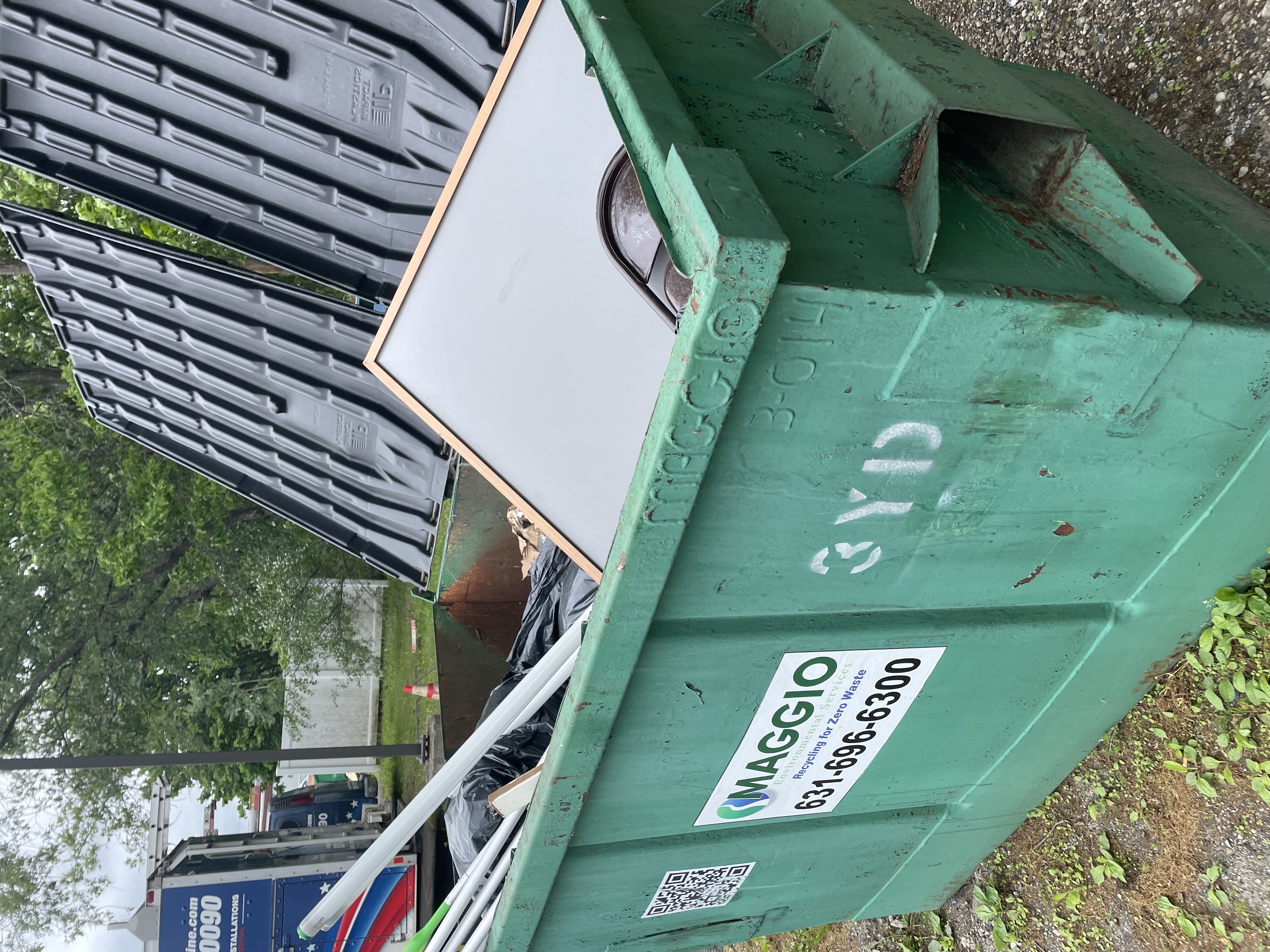 Green commercial dumpster filled with debris and a white board