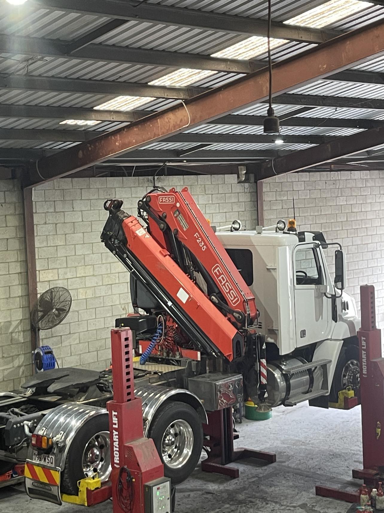 White truck with Fassi crane on workshop lift