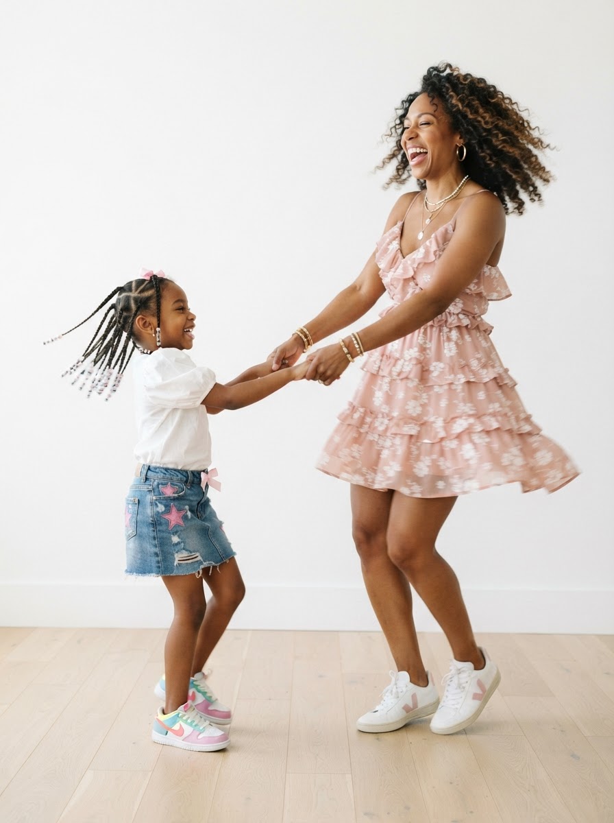 A stylish Black mother and her daughter laughing and dancing together in coordinated pink outfits