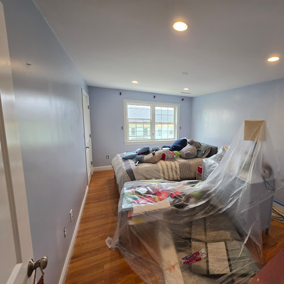 Light blue room with bed covered in plastic for painting prep