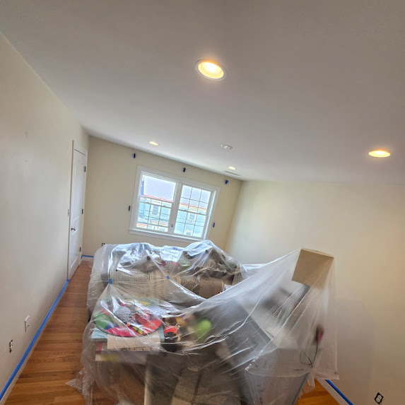Beige room with bed covered in plastic for painting prep