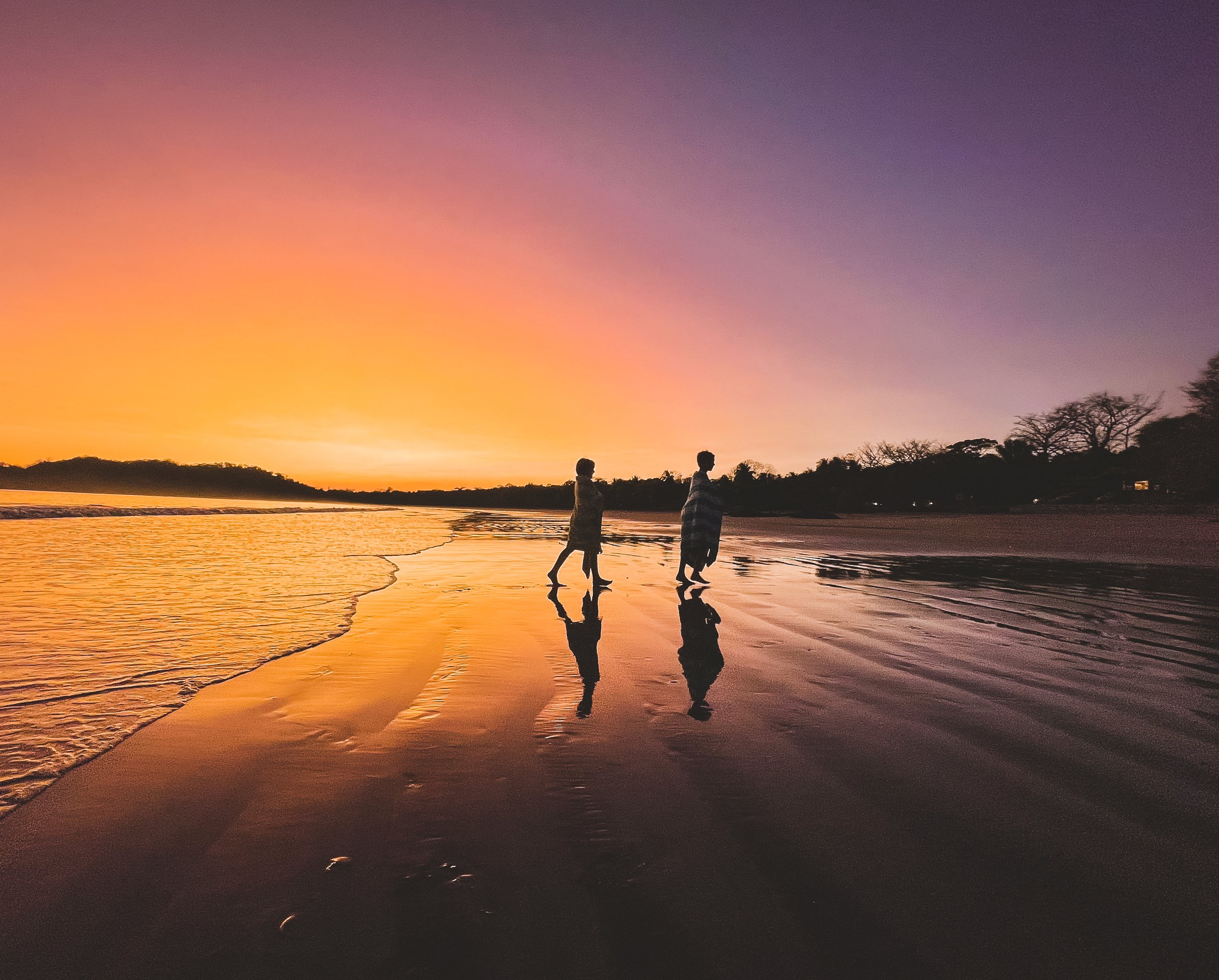 Children walking along the shoreline at golden-hour sunset in Costa Rica