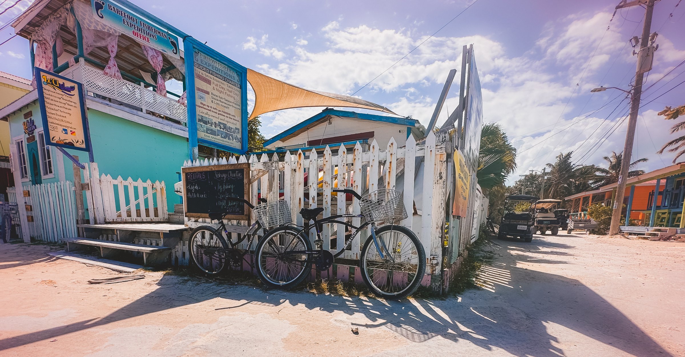 Bicycles parked on a sandy street next to a white picket fence