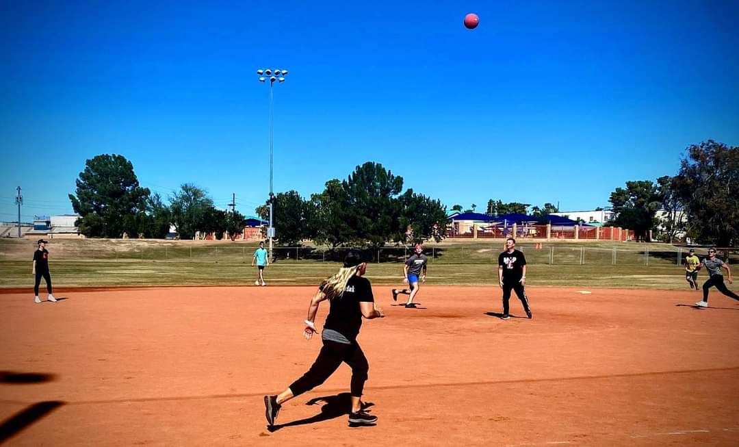 High-flying kickball popup against clear Arizona blue sky with players tracking