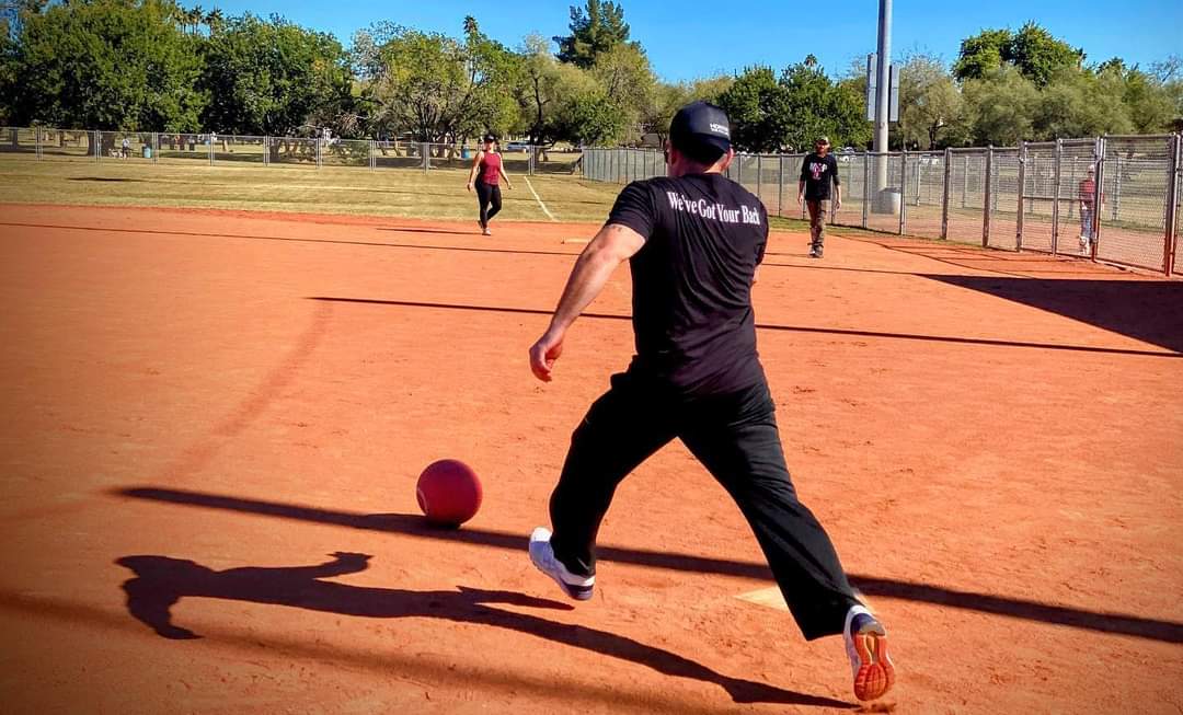 Pitcher delivering the ball on the dirt diamond with We've Got Your Back jersey