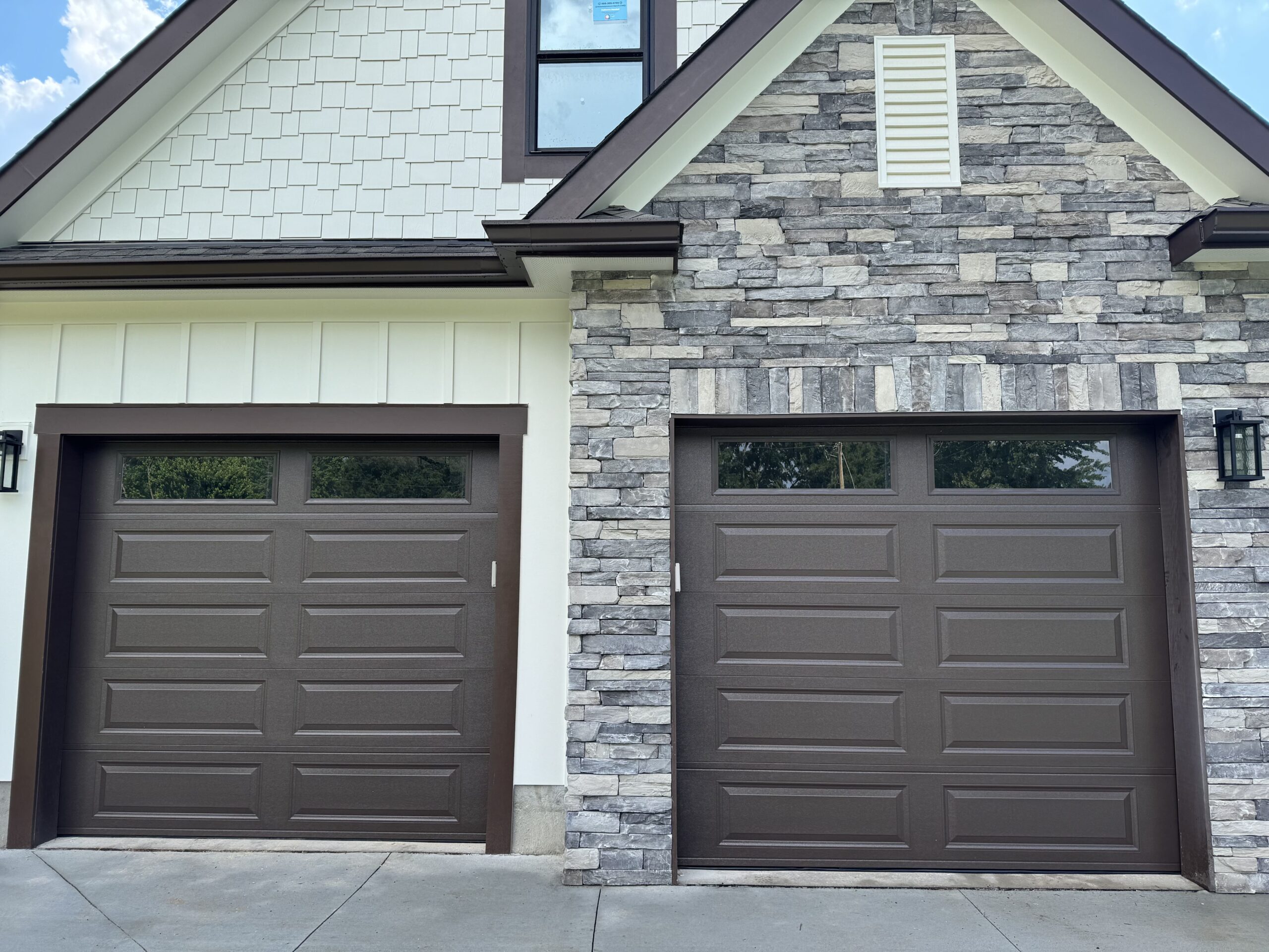 Pair of dark brown steel garage doors with glass inserts installed by Garage Door Gators on a stone-facade home in Mint Hill NC — repair and replacement services available