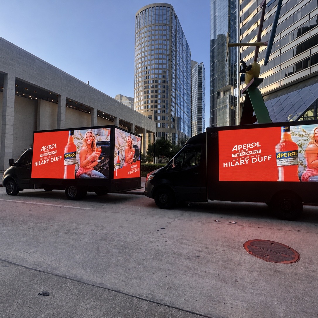 Motivo Mobile Billboards LED truck displaying a daytime advertising campaign on bright downtown Houston streets near skyscrapers