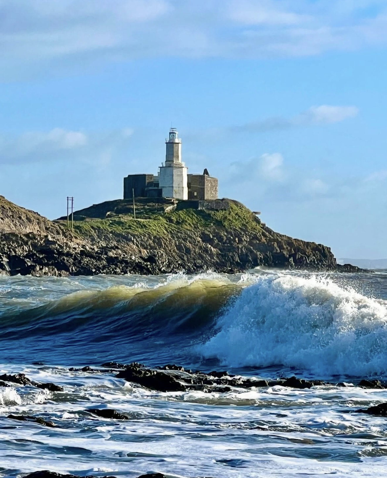 Mumbles Lighthouse standing on the rocky headland with rolling waves in Swansea Bay