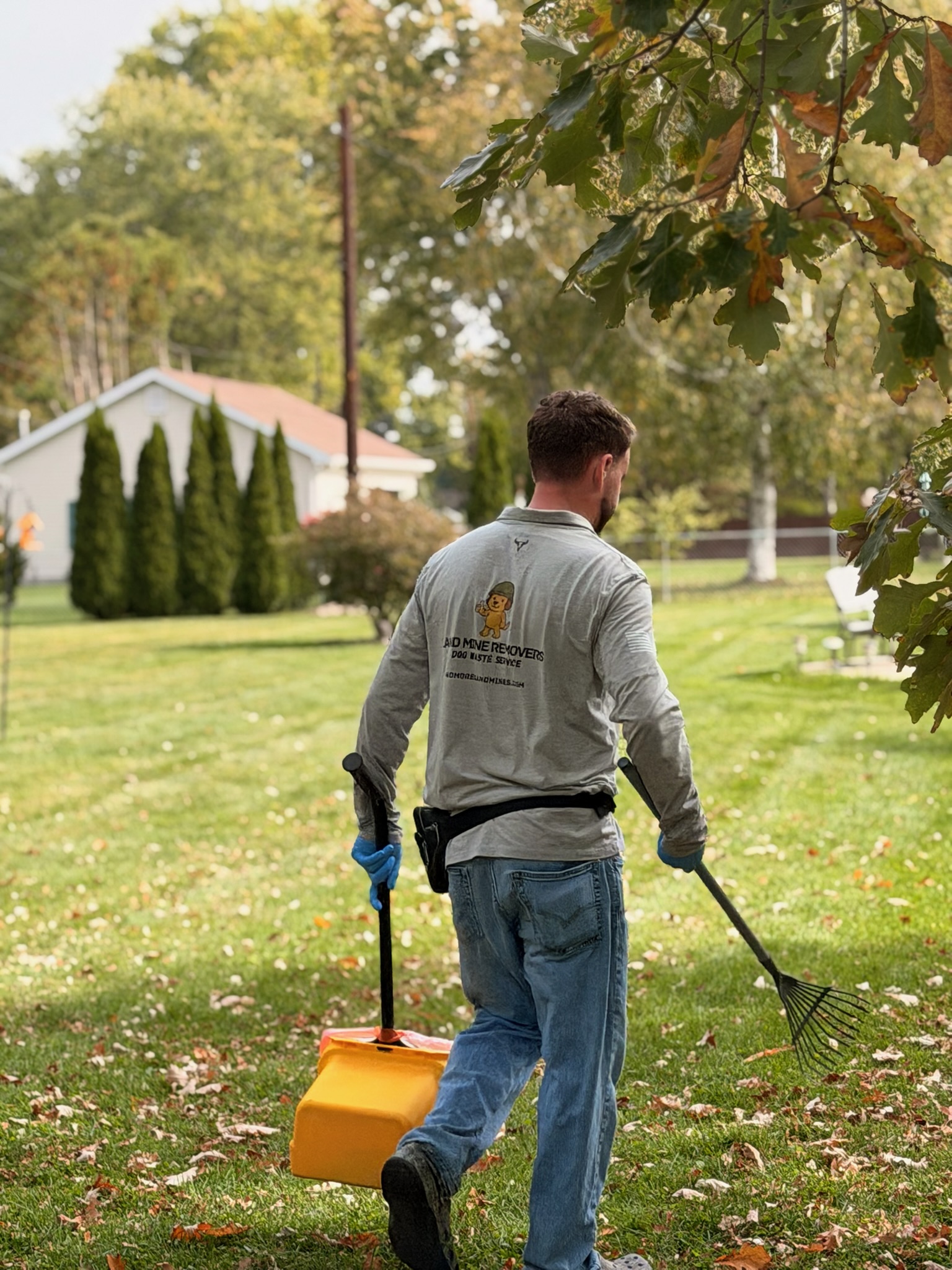 Technician actively scooping dog waste across a spacious Michigan lawn