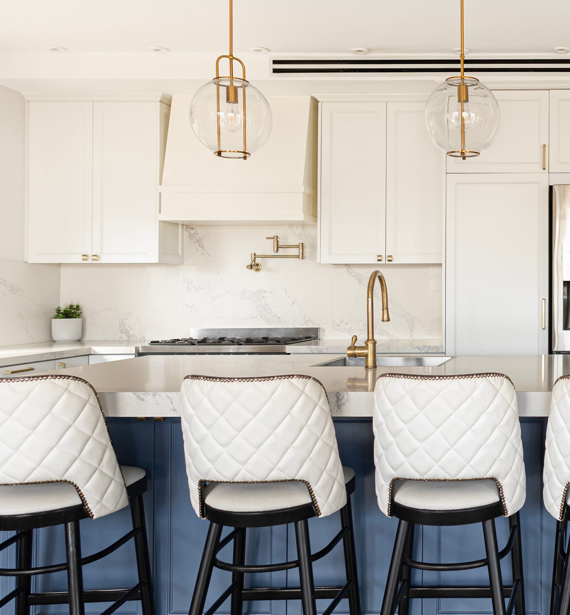 Kitchen with white cabinets, blue island, and white quilted bar stools