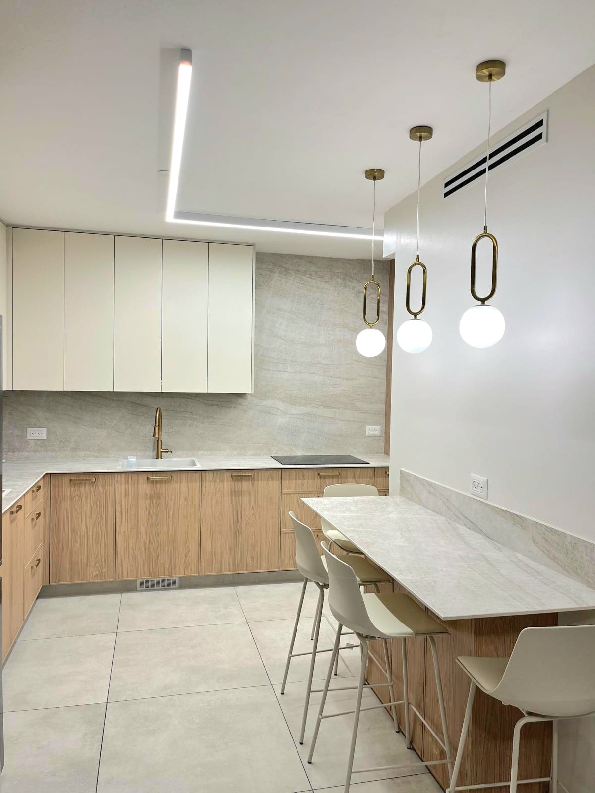 Open plan kitchen with white upper cabinets and wood lower cabinets with gold faucet