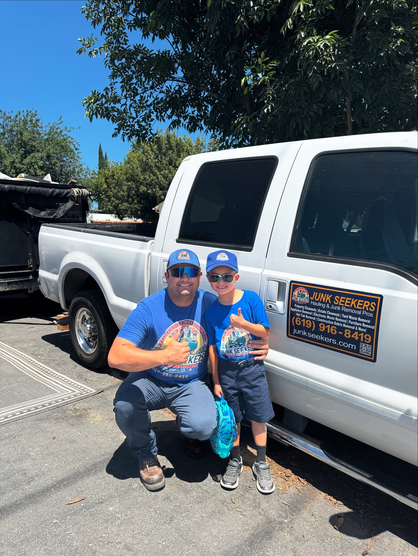 Junk Seekers owner Santiago and his son smiling warmly in front of their branded service truck