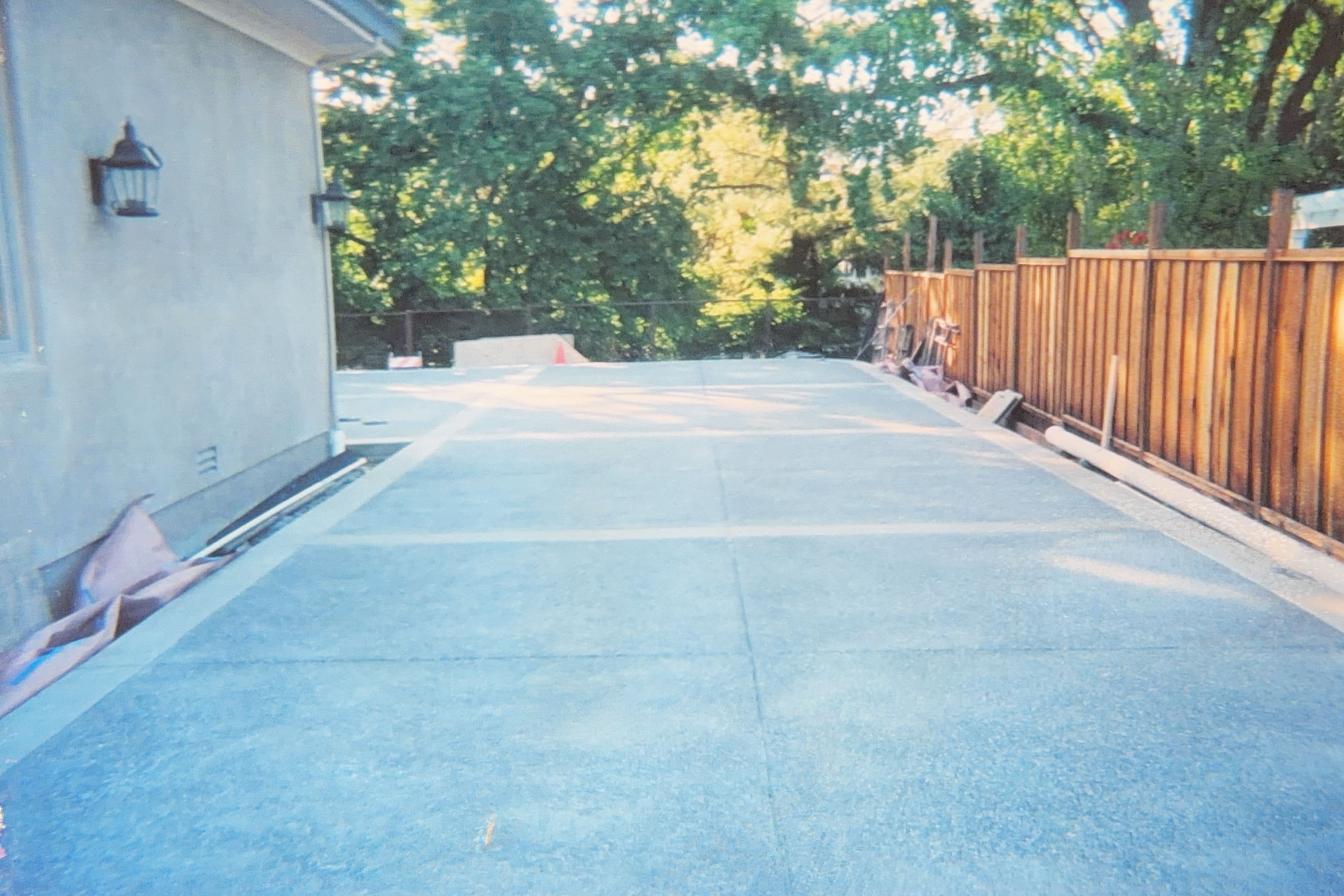Newly poured concrete driveway or patio beside a house with a wooden fence