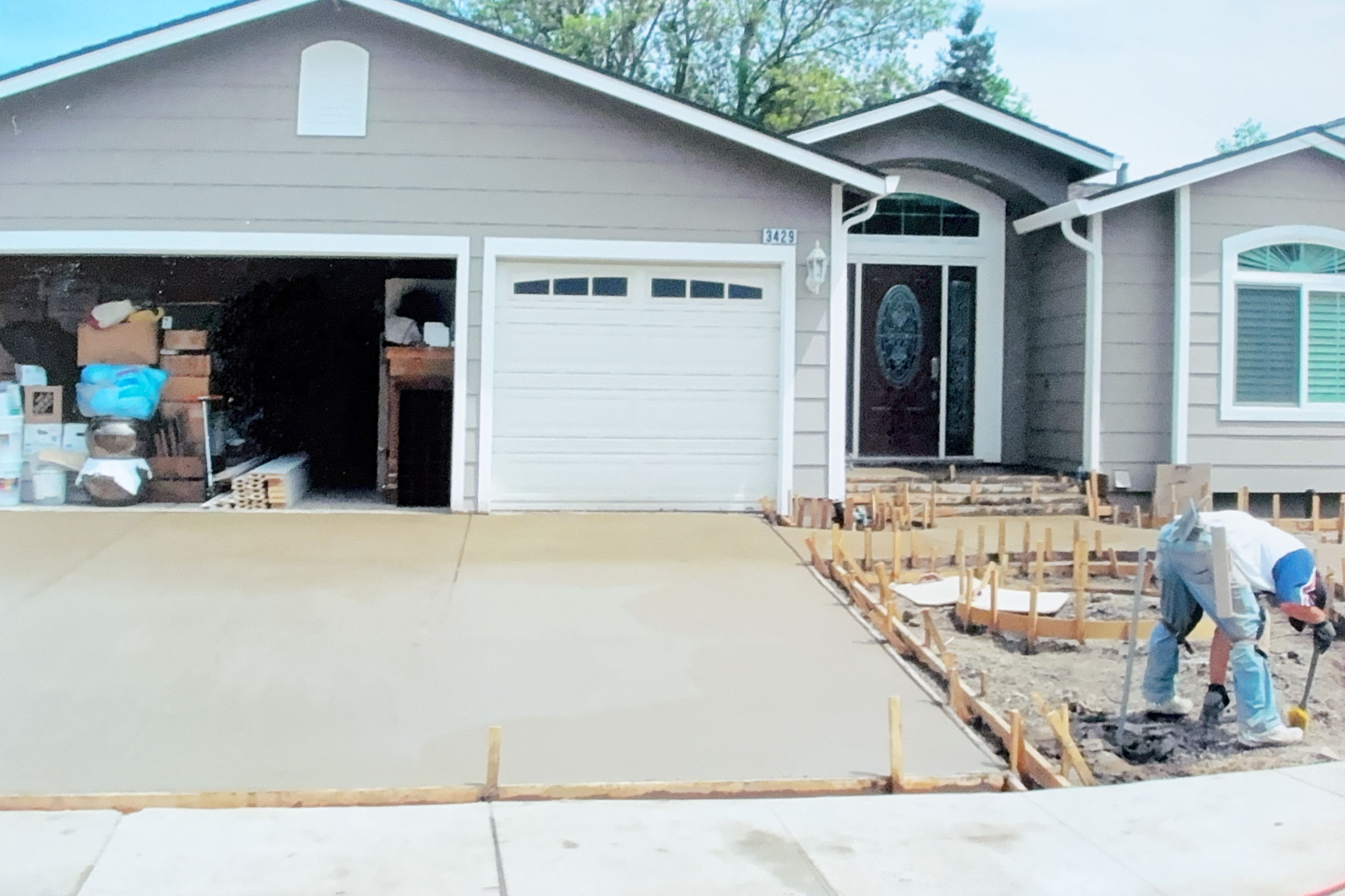 Worker smoothing a newly poured concrete driveway in front of a house