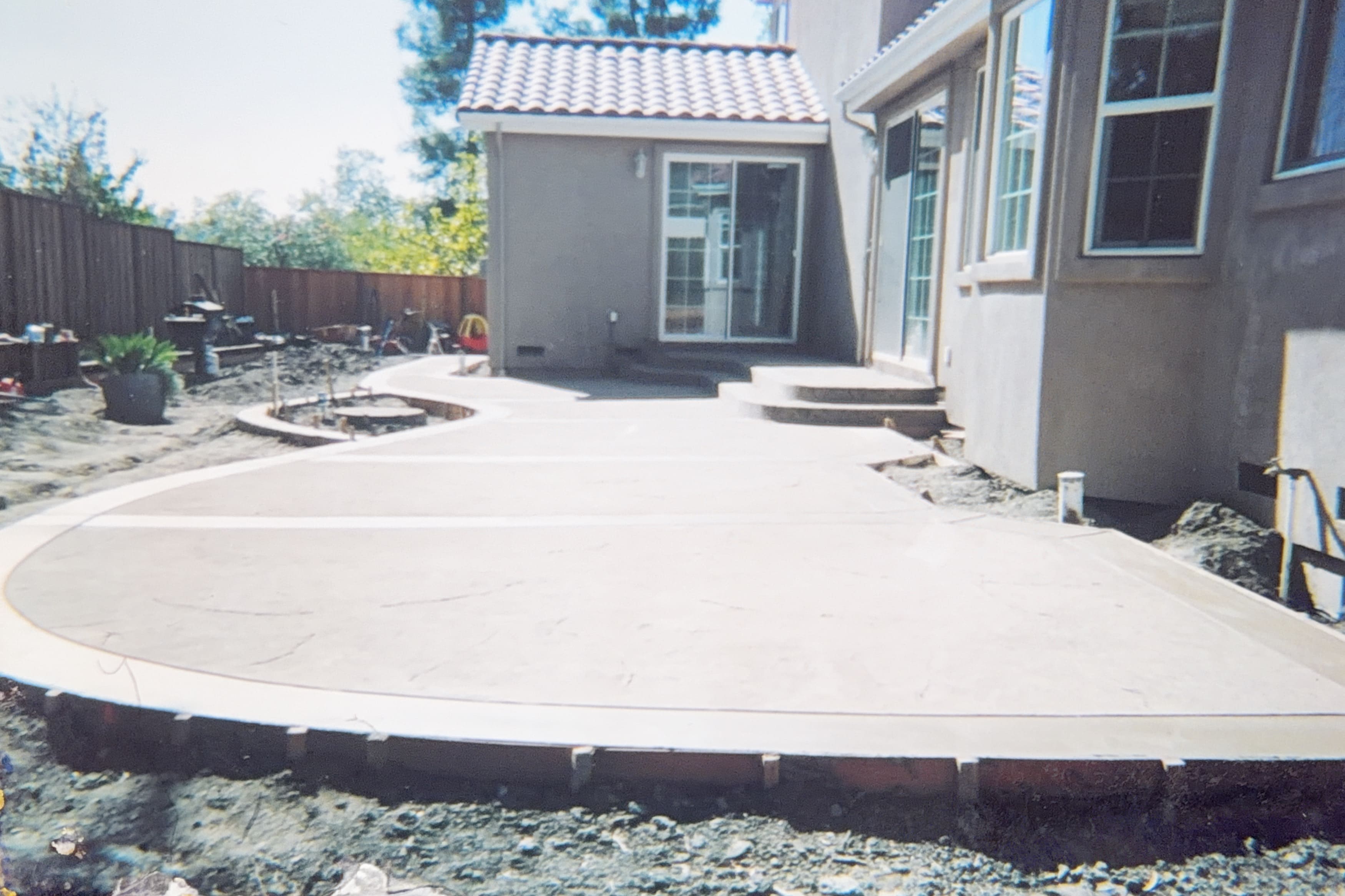 A large concrete patio under construction in a backyard, with a curved edge and a circular fire pit area