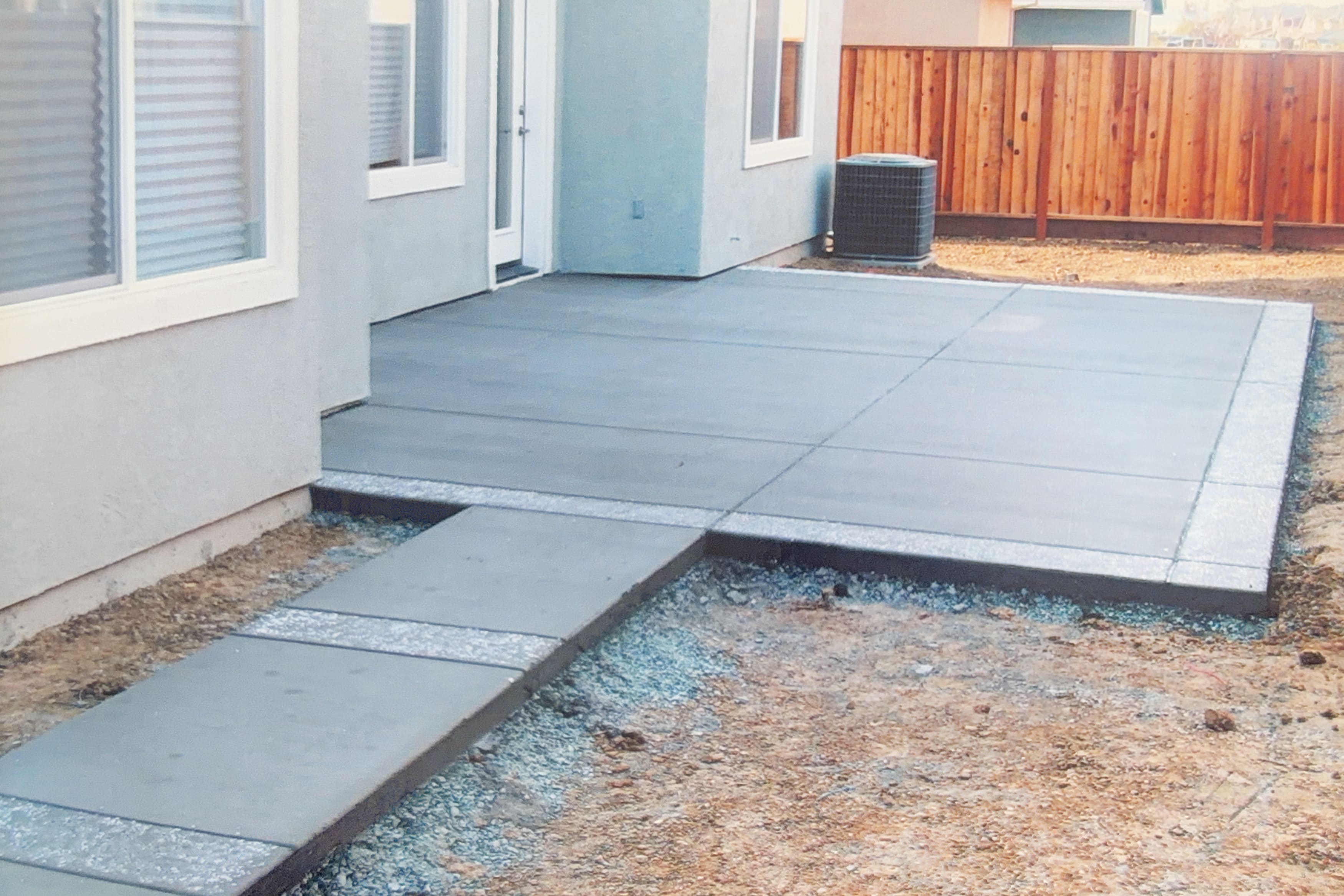 Newly poured concrete patio in a backyard with a wooden fence