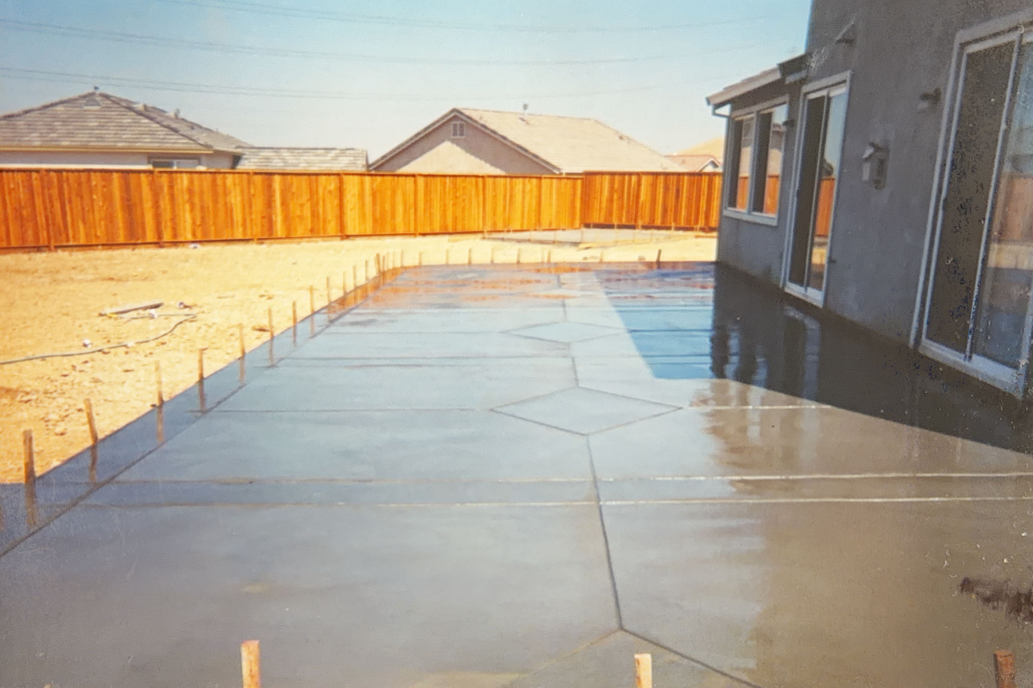 Large freshly poured concrete patio with wooden forms and diamond scoring pattern