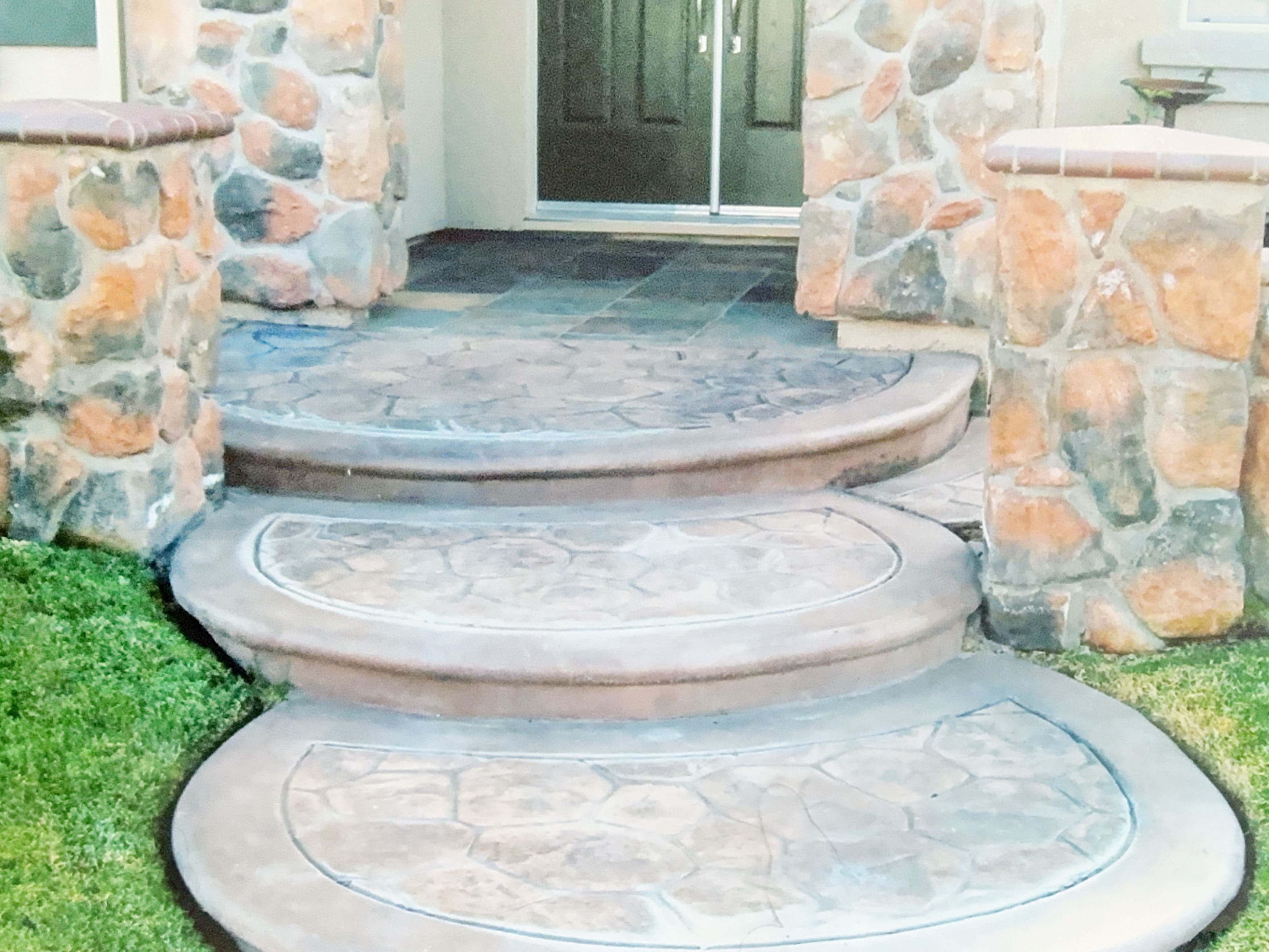 Stamped concrete steps leading to a front door, flanked by stone pillars