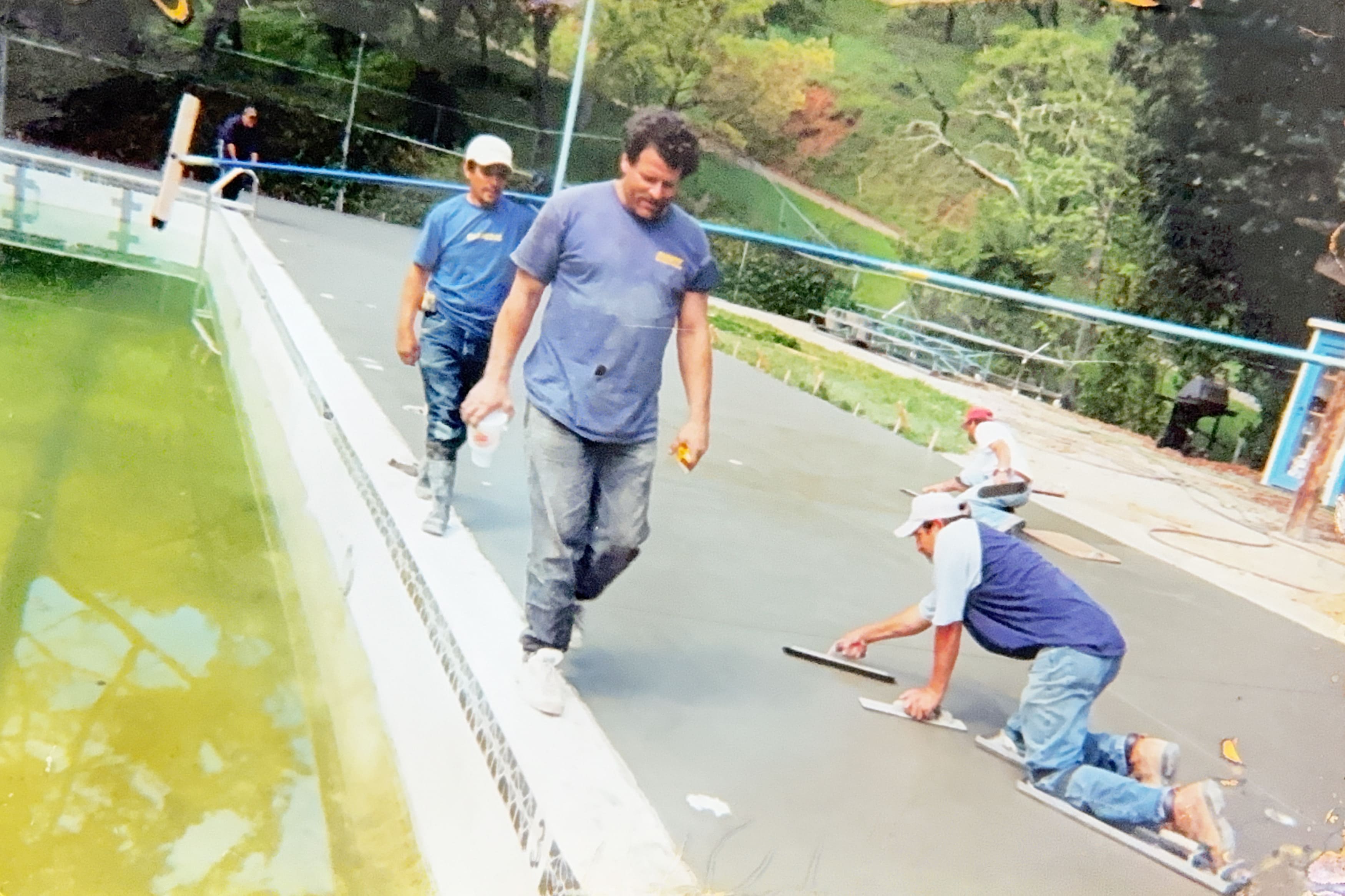 Workers smoothing freshly poured concrete around a large swimming pool