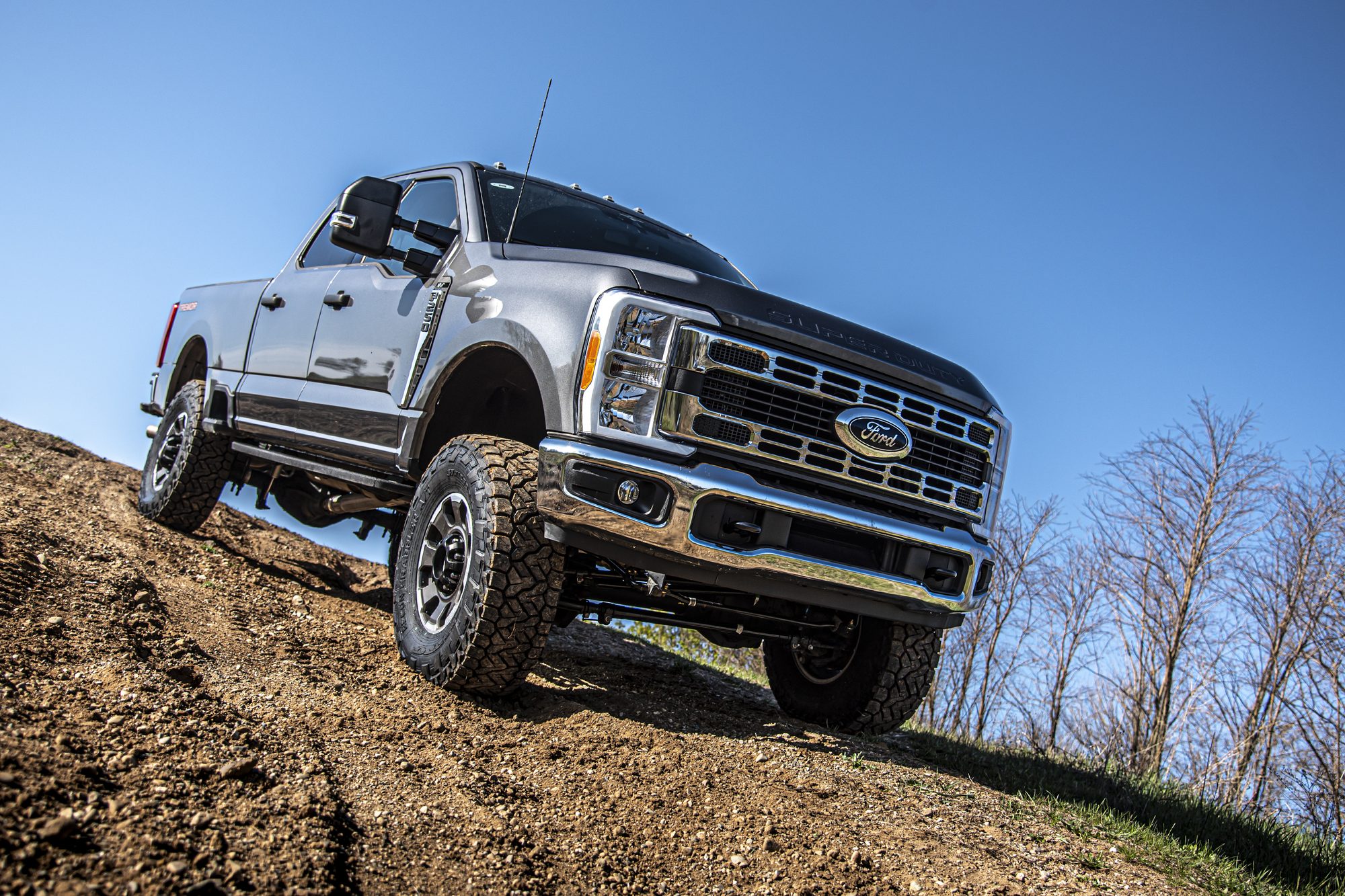 Gray lifted Ford Super Duty on aftermarket wheels climbing a dirt mound