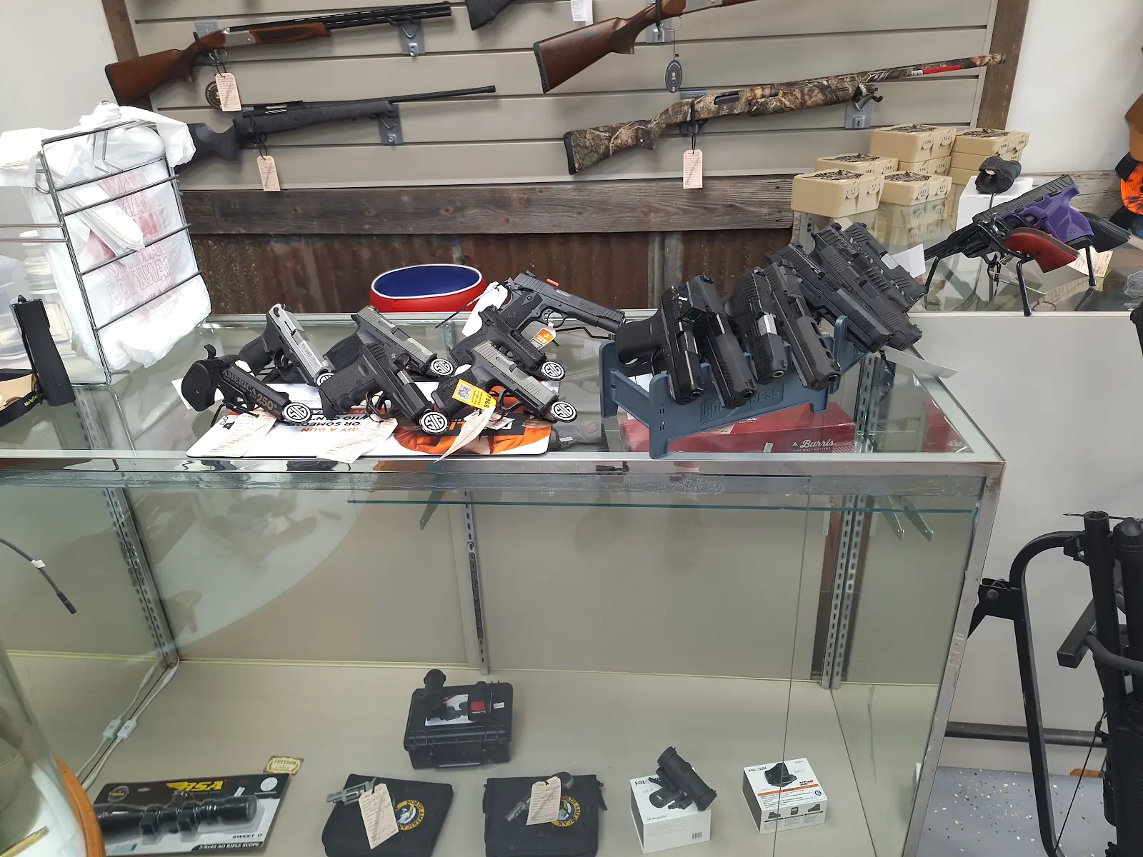 Handguns and revolvers displayed on a glass counter with long firearms mounted on the wall inside Freedom Forever Firearms in Manistique, Michigan.