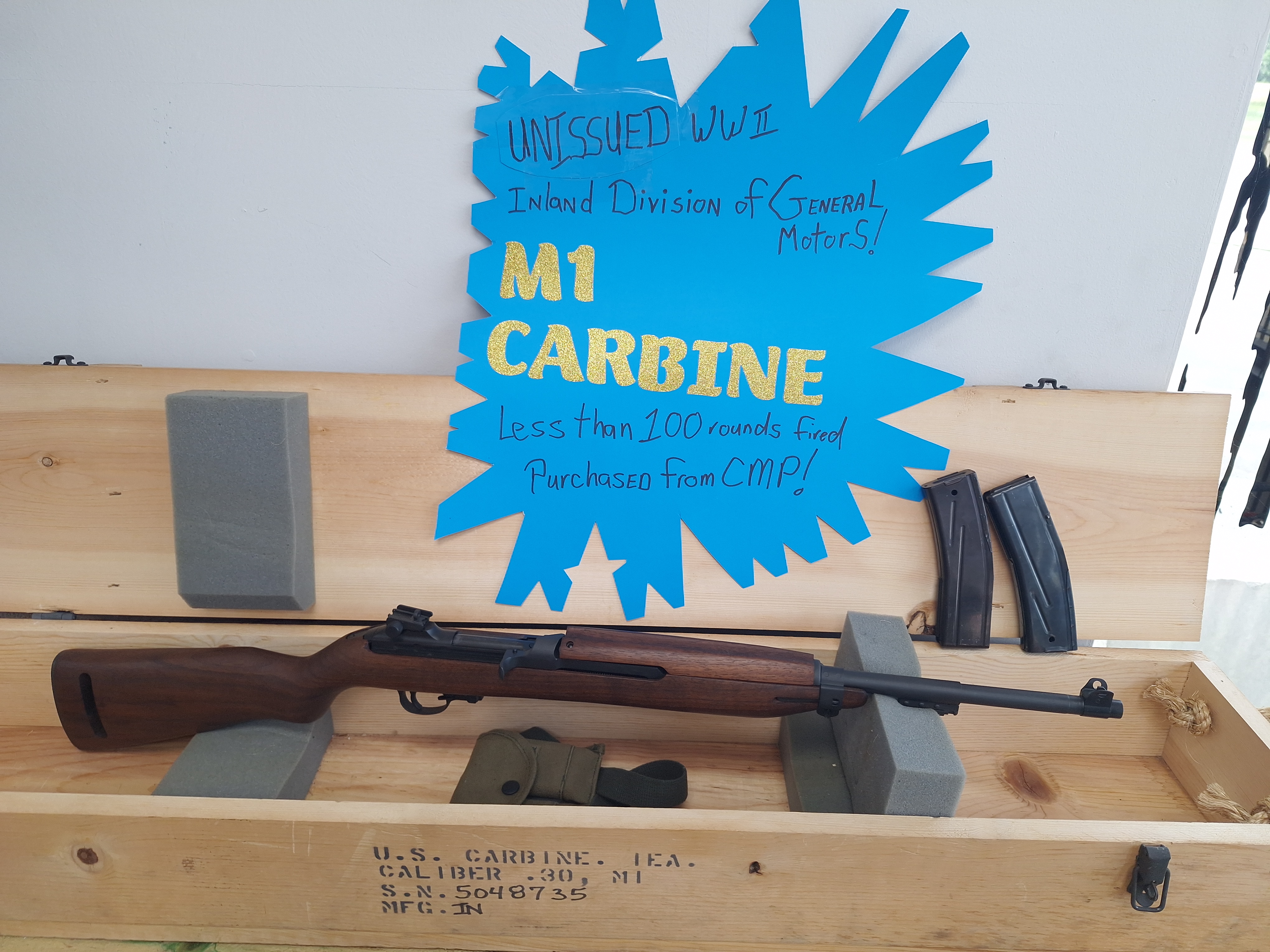 Historic M1 Carbine displayed in a wooden presentation case with magazines and informational store signage.