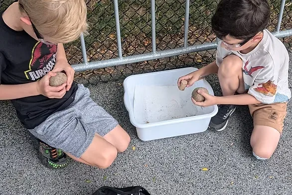 Two children crouched outdoors examining rocks over a tray of water