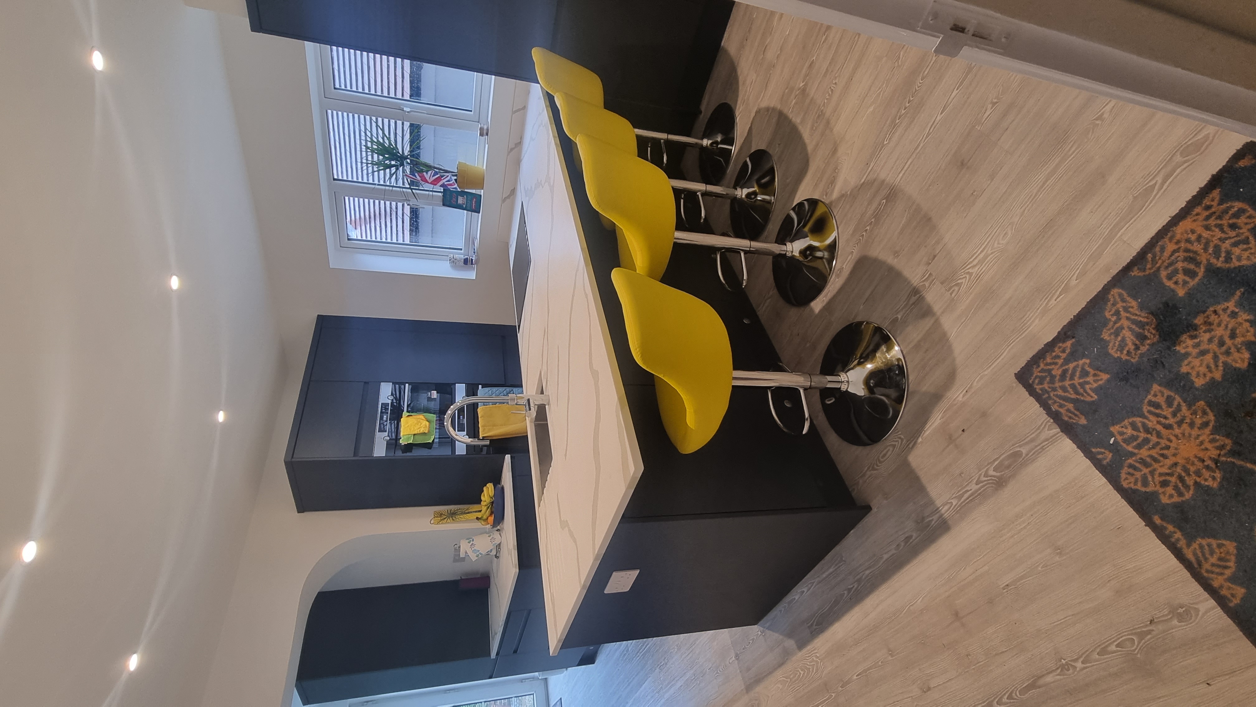 Modern white quartz kitchen island with breakfast bar seating and vibrant yellow stools