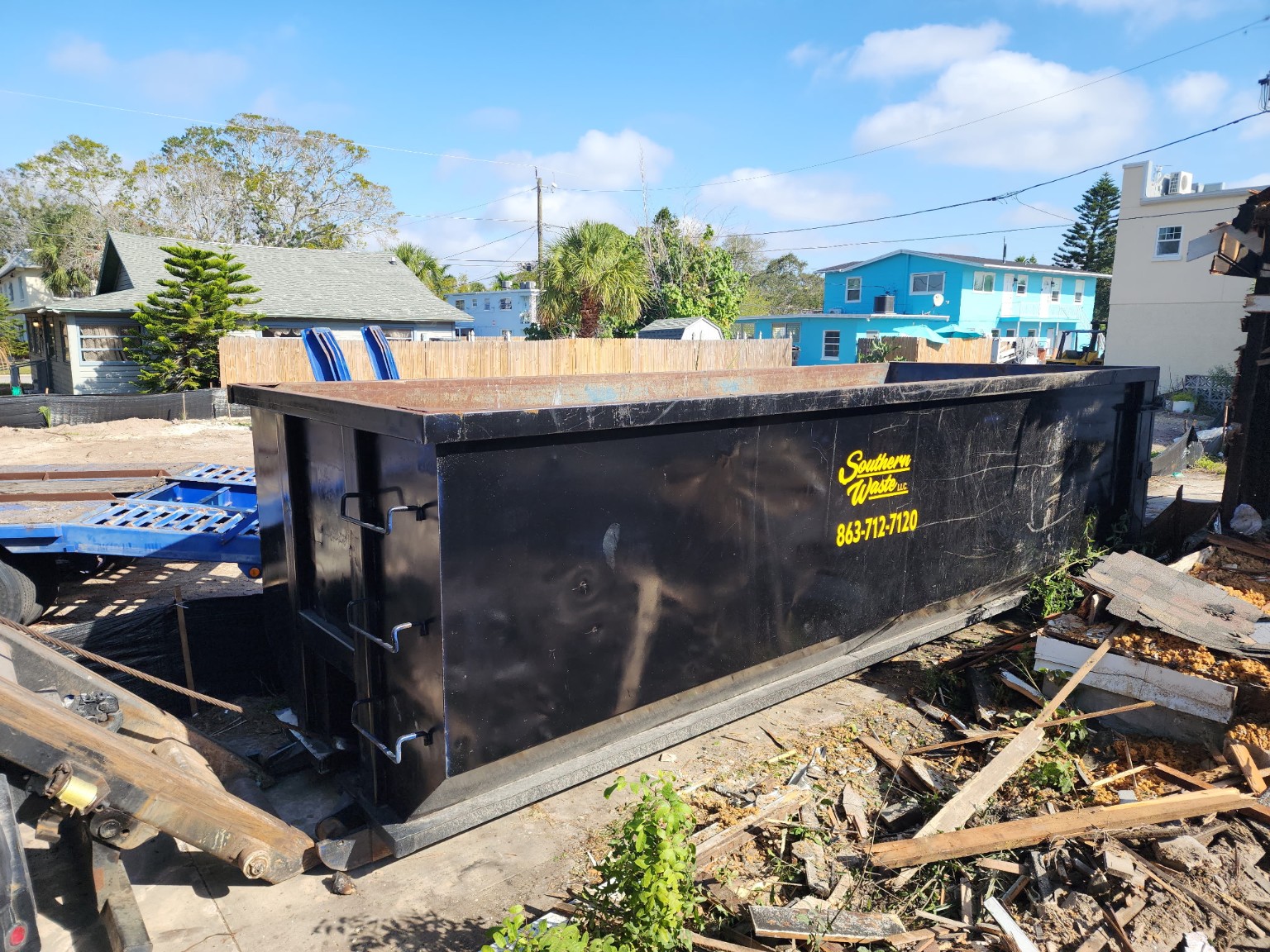 Black roll-off dumpster on site at a residential demolition cleanup job collecting construction debris