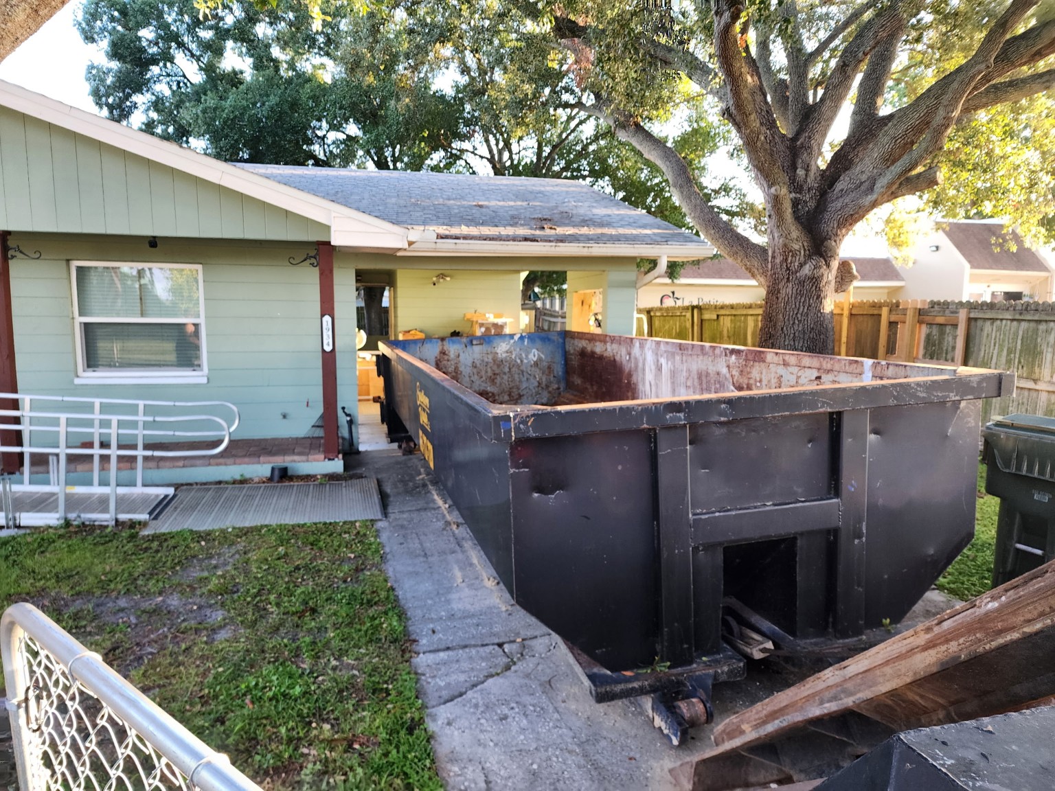 Large black roll-off dumpster placed in a residential driveway for home cleanout and remodeling project