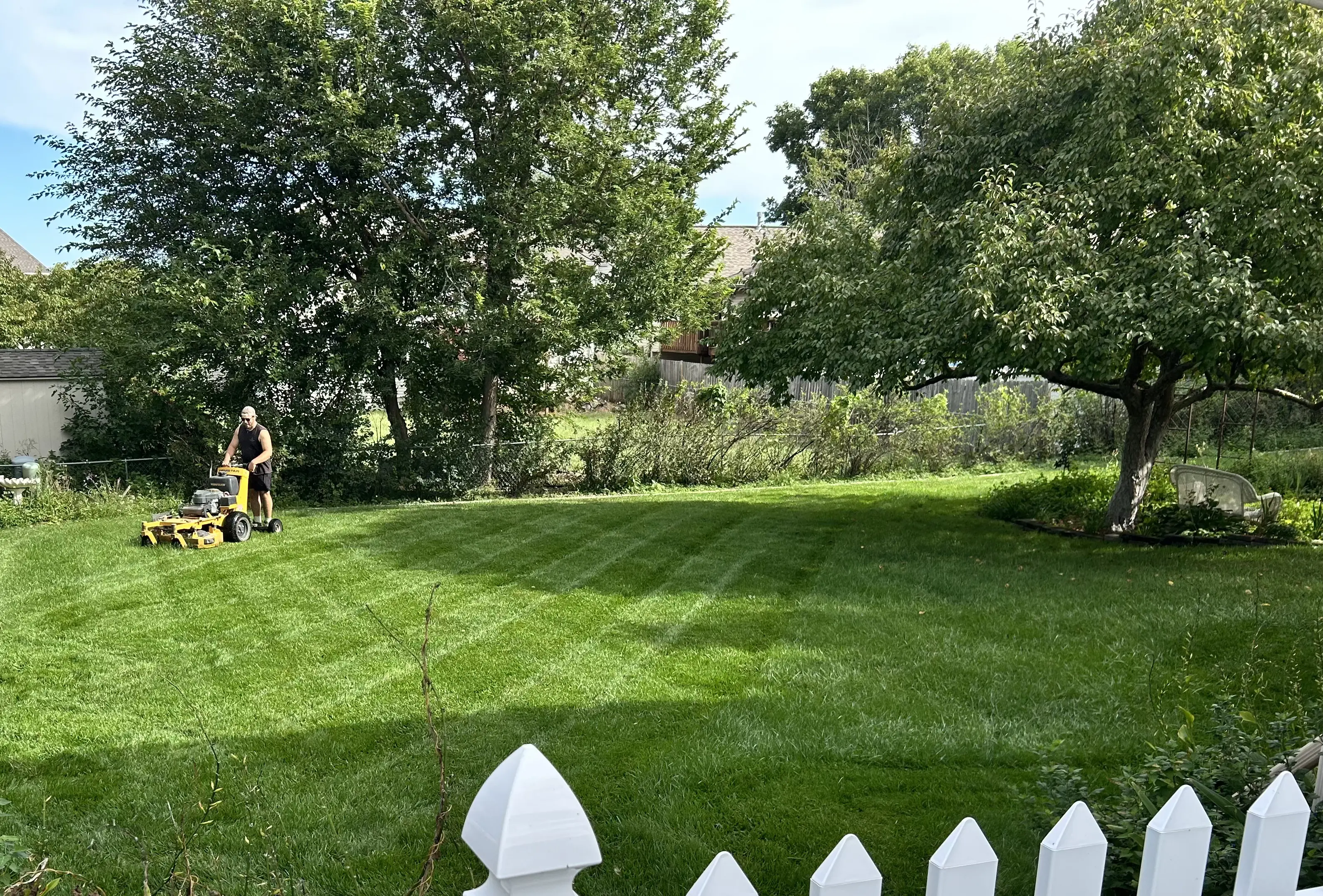 Residential lawn mowing with clean cut lines behind white fence in Lincoln, NE