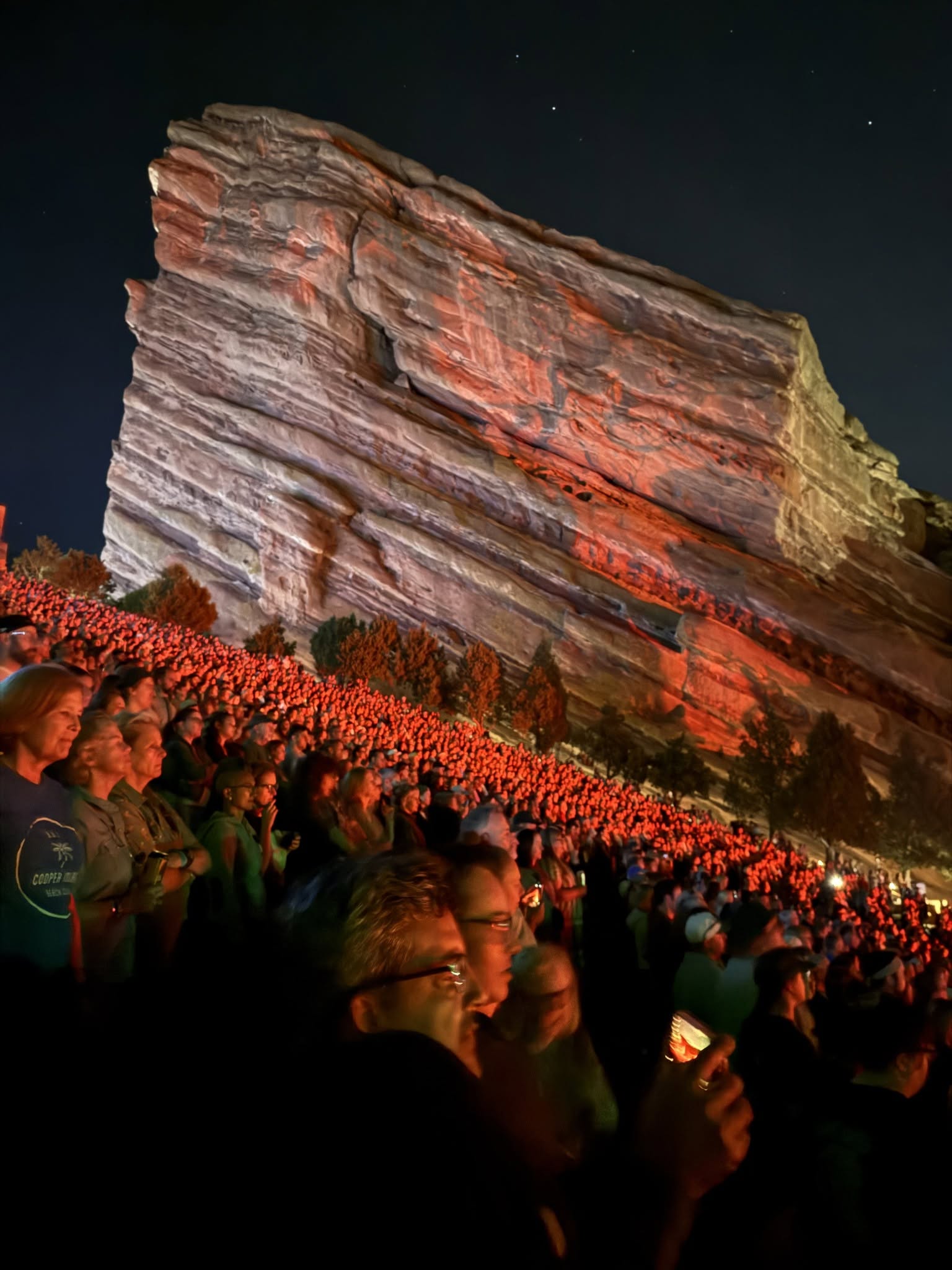 The iconic Red Rocks sandstone illuminated in brilliant crimson red above the packed crowd